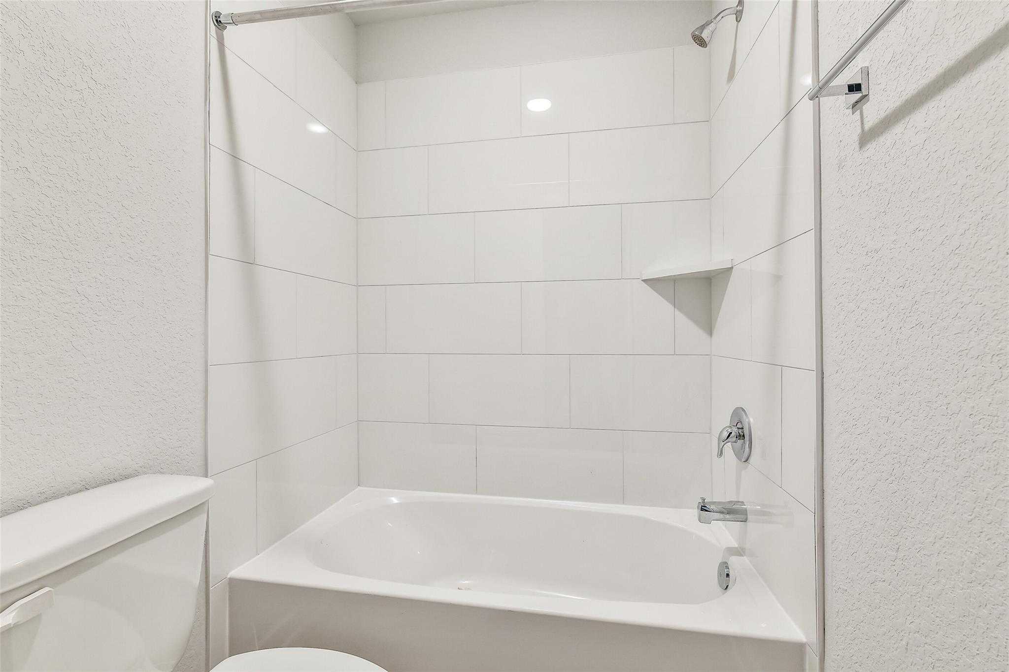 Modern white subway tile shower with glass door, soaking tub, and toilet in Davidson Homes The Blanco E bathroom, Magnolia, Texas