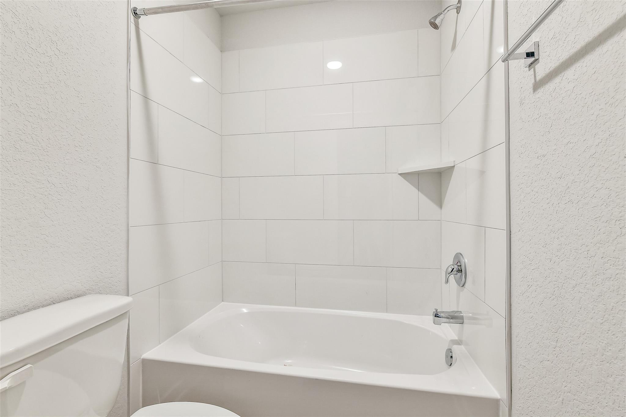 Modern white subway tile shower with glass door, soaking tub, and toilet in Davidson Homes The Blanco E bathroom, Magnolia, Texas