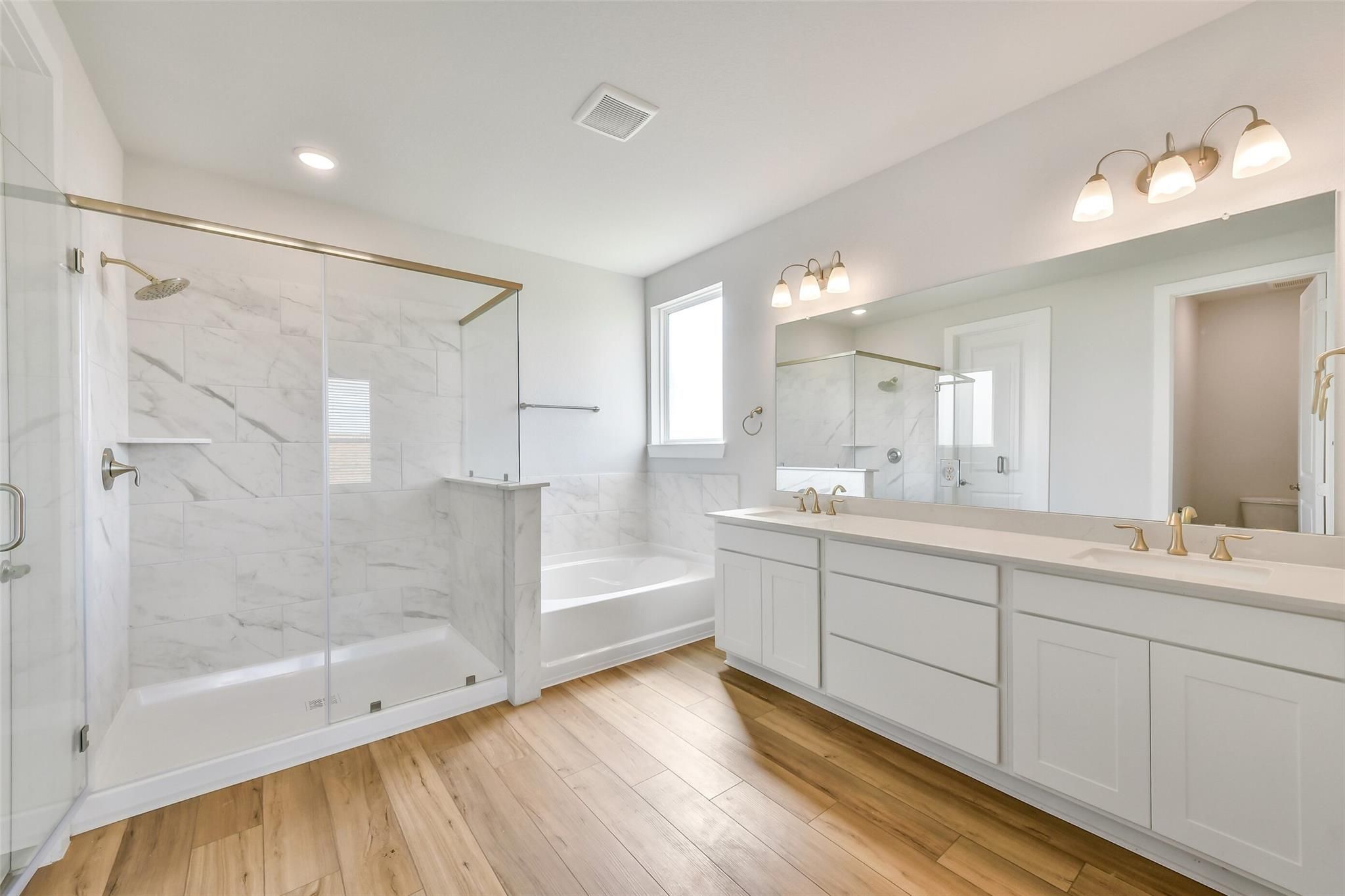 Luxurious master bathroom featuring marble glass shower, freestanding tub, double vanity with gold fixtures in Davidson Homes The Victoria A, Lago Mar