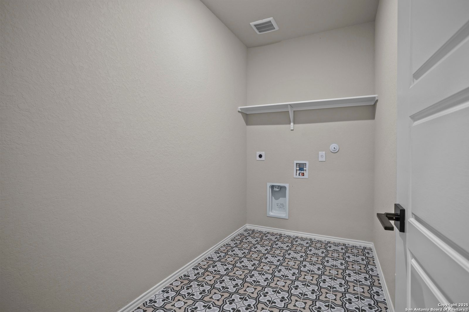 Laundry room with beige walls, built-in white shelves, washer-dryer hookups, and patterned tile floor in Davidson Homes Douglas F, San Antonio