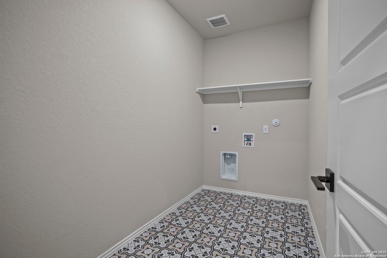 Laundry room with beige walls, built-in white shelves, washer-dryer hookups, and patterned tile floor in Davidson Homes Douglas F, San Antonio