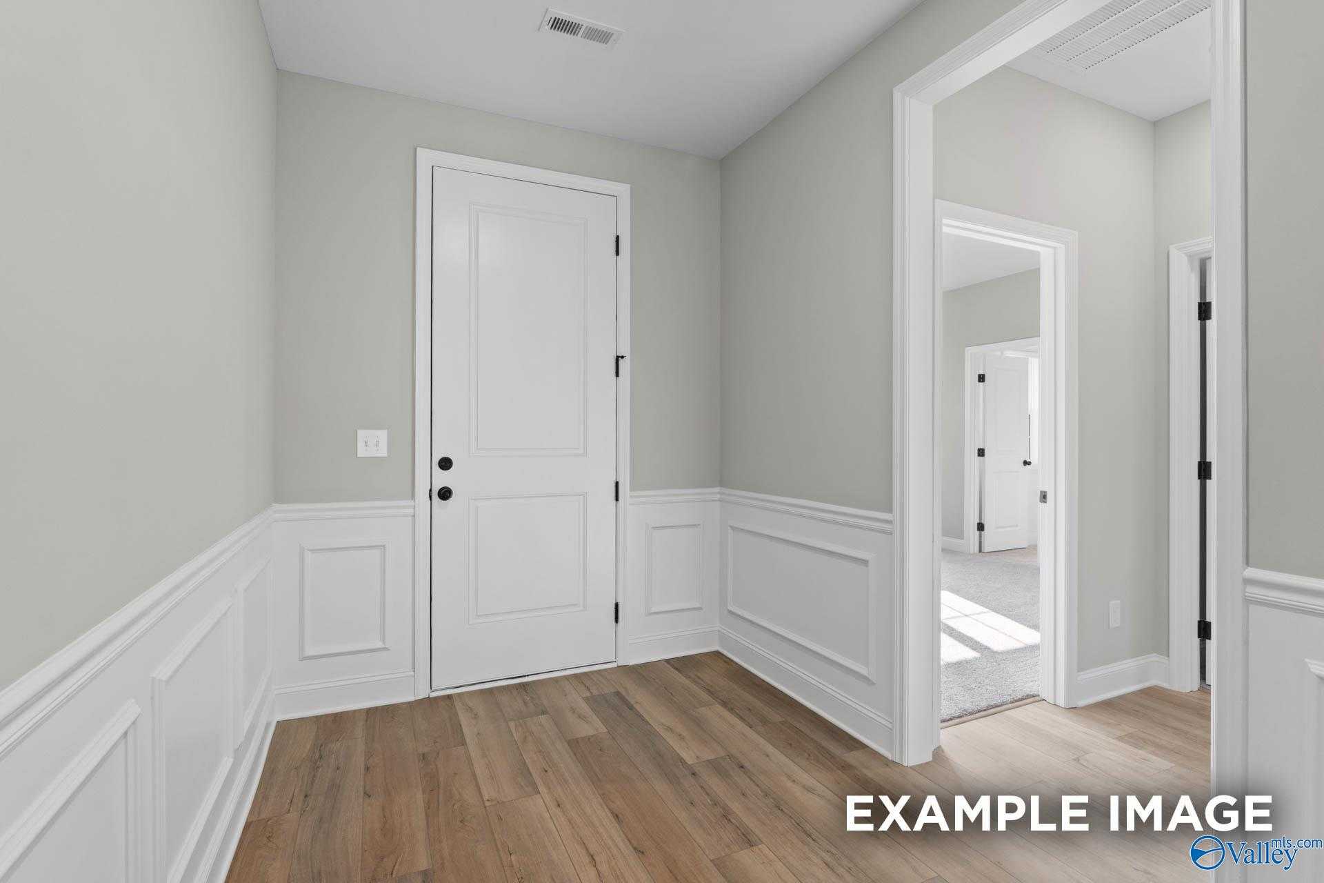 Elegant hallway with white paneled doors, neutral gray walls, and hardwood floors in Davidson Homes Montgomery B, Toney, AL