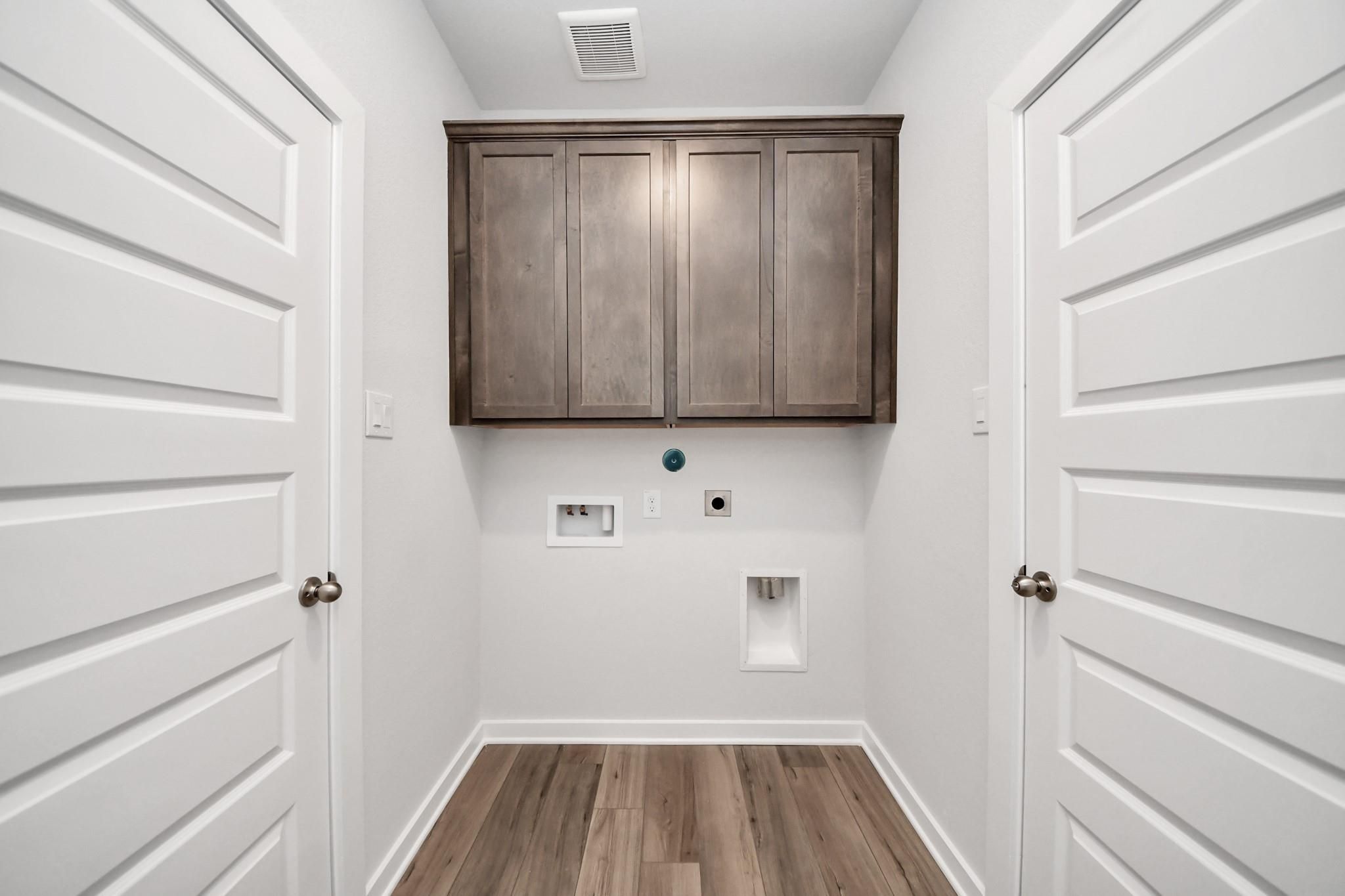 Laundry room with wood-look flooring and overhead cabinets in The Sabine E floor plan at Liberty Estates, Cleveland, Texas.