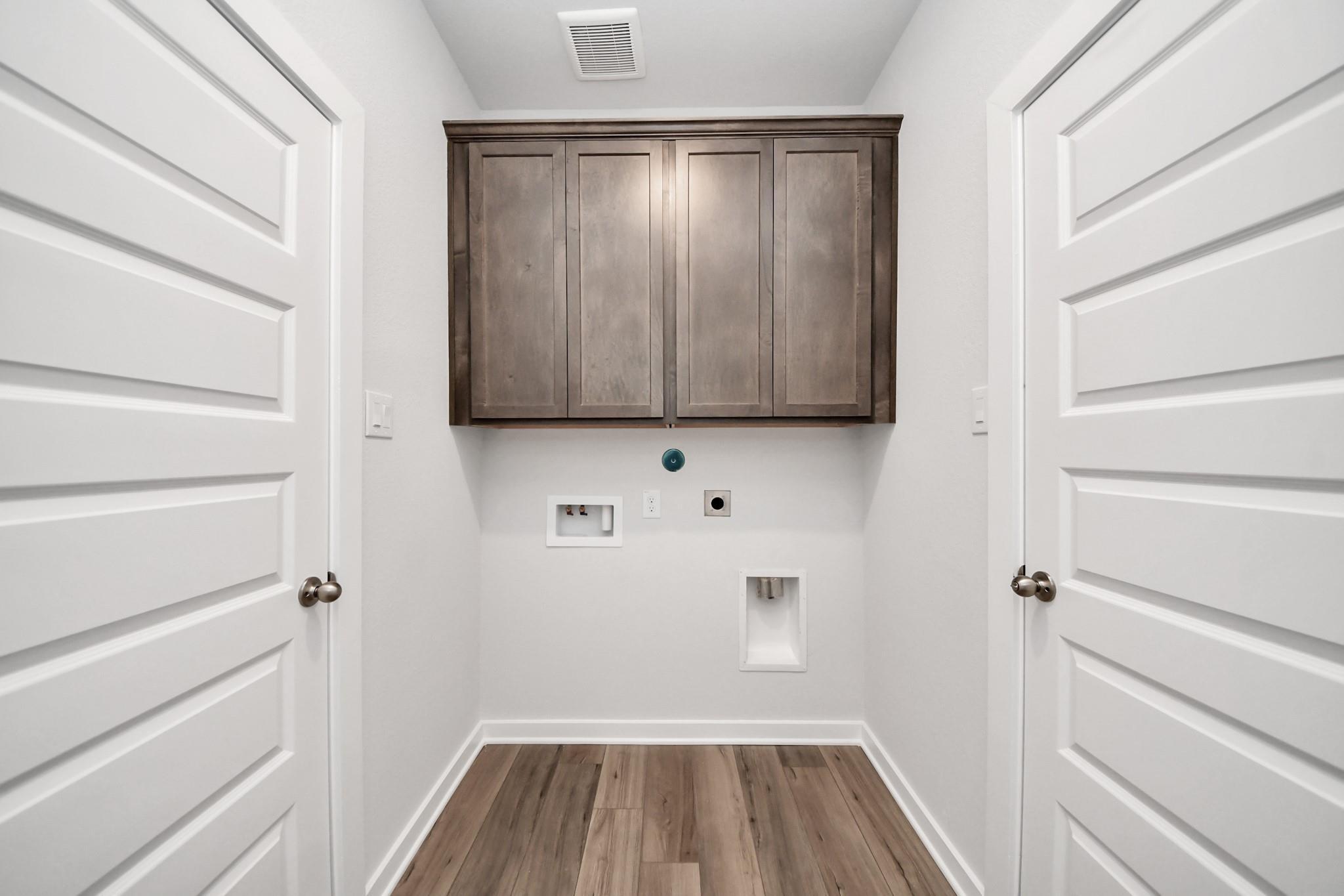 Laundry room with wood-look flooring and overhead cabinets in The Sabine E floor plan at Liberty Estates, Cleveland, Texas.