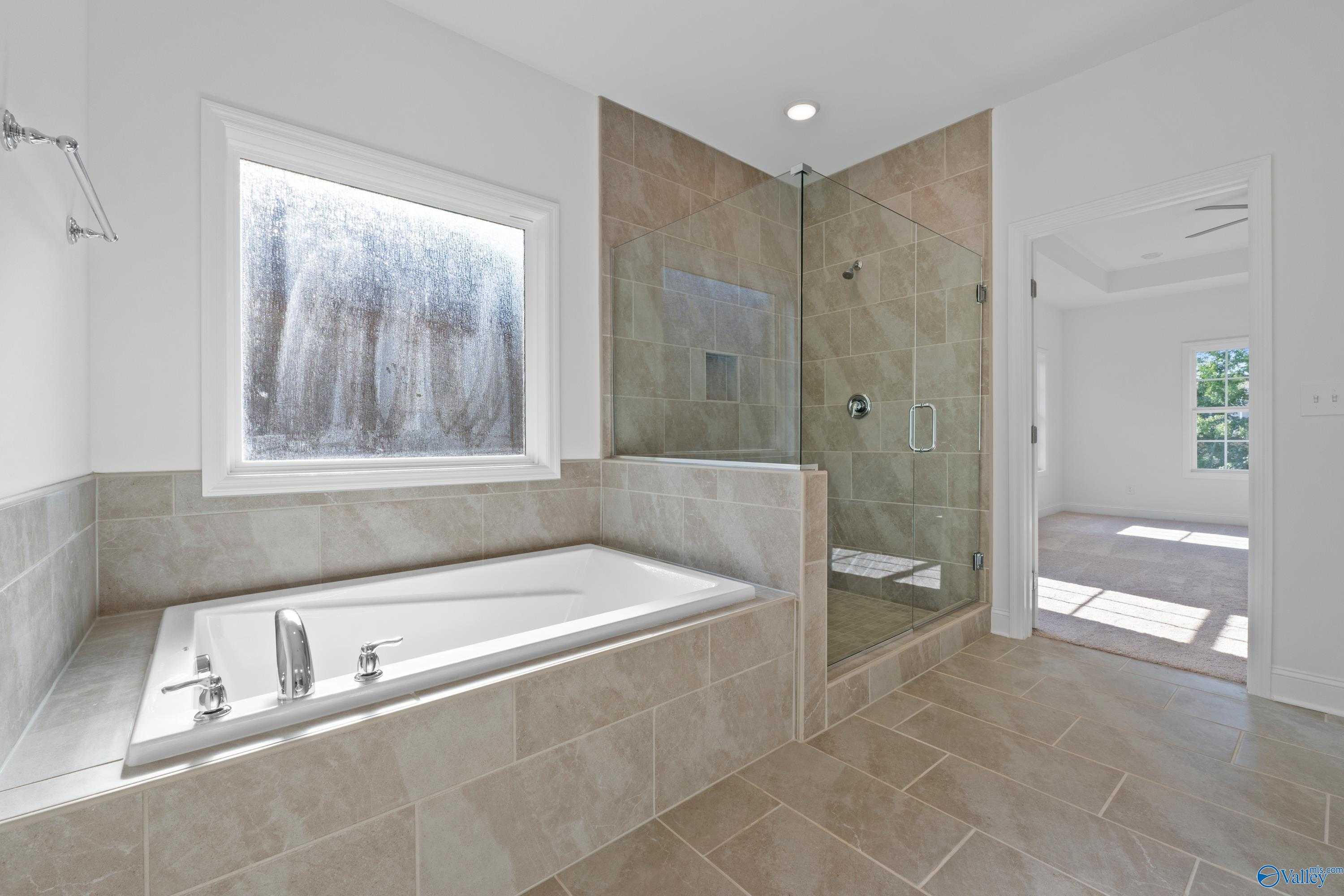 Elegant master bathroom featuring freestanding tub, glass shower, and tiled floors in Davidson Homes The Oxford, Harvest, AL