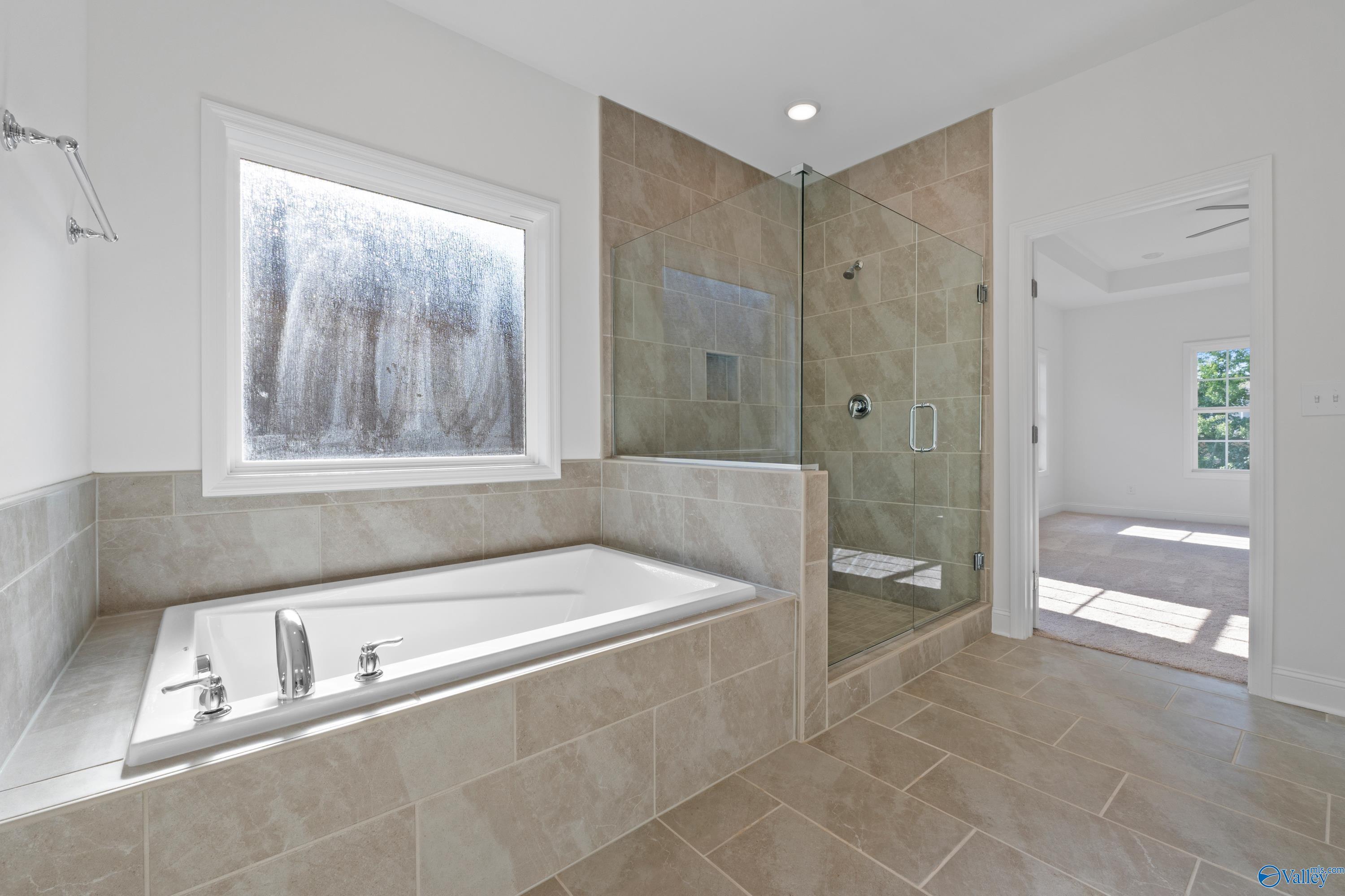 Elegant master bathroom featuring freestanding tub, glass shower, and tiled floors in Davidson Homes The Oxford, Harvest, AL