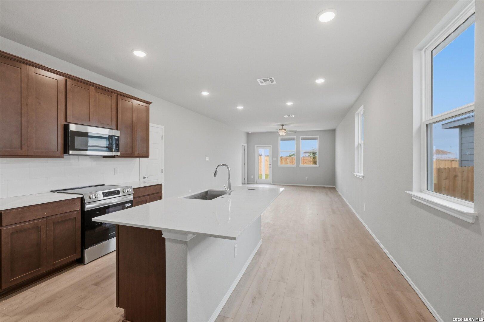 Modern kitchen featuring white quartz counters, stainless steel appliances, brown shaker cabinets, open to living area in Davidson Homes The Frio B, San Antonio