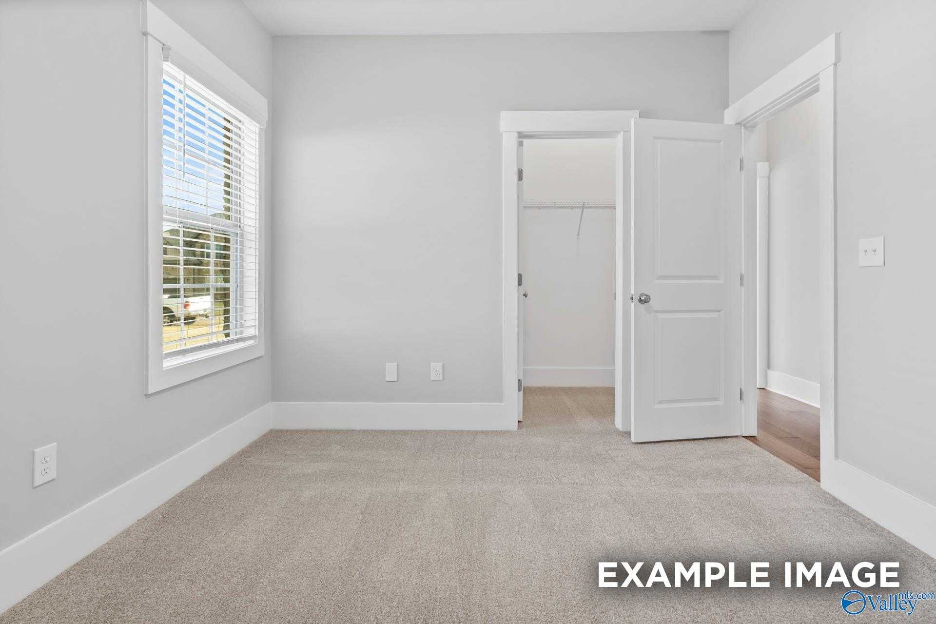 Bright bedroom with walk-in closet, large window blinds, and neutral gray walls in Davidson Homes The Rockford, Meridianville, Alabama