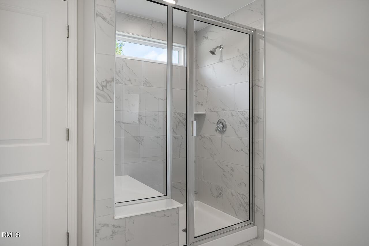 Elegant frameless glass shower with white marble tiles, built-in bench, and window in master bath of Davidson Homes The Graham in Fuquay-Varina, NC