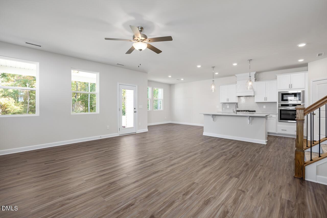 Open-concept living room and kitchen with hardwood floors, white cabinets, island, and staircase in The Grace C by Davidson Homes, Lillington, NC