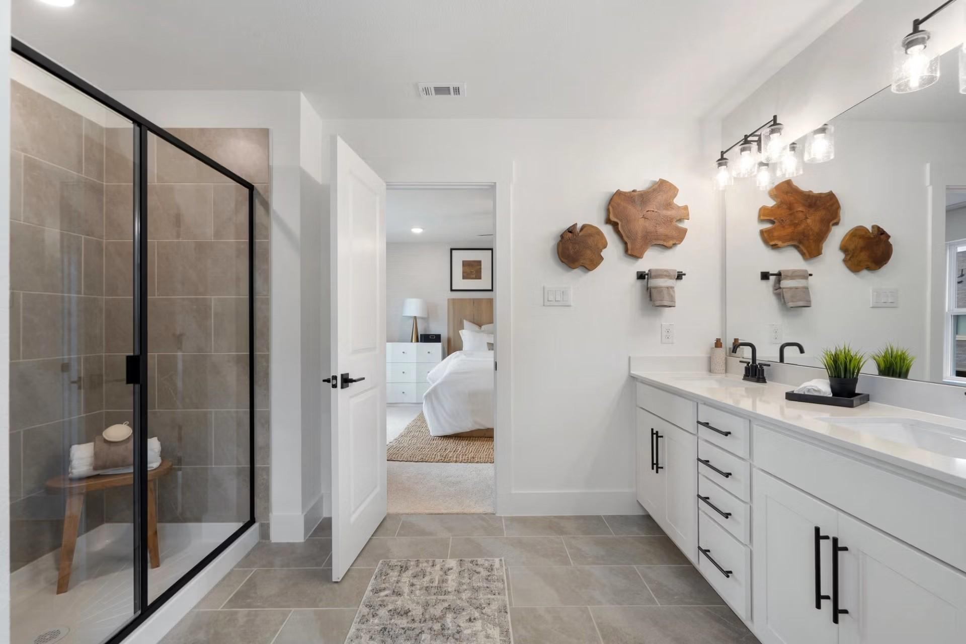 Modern master bathroom with glass shower, double vanity, wood wall art, and open bedroom view in Davidson Homes The Wake D, Wylie, TX
