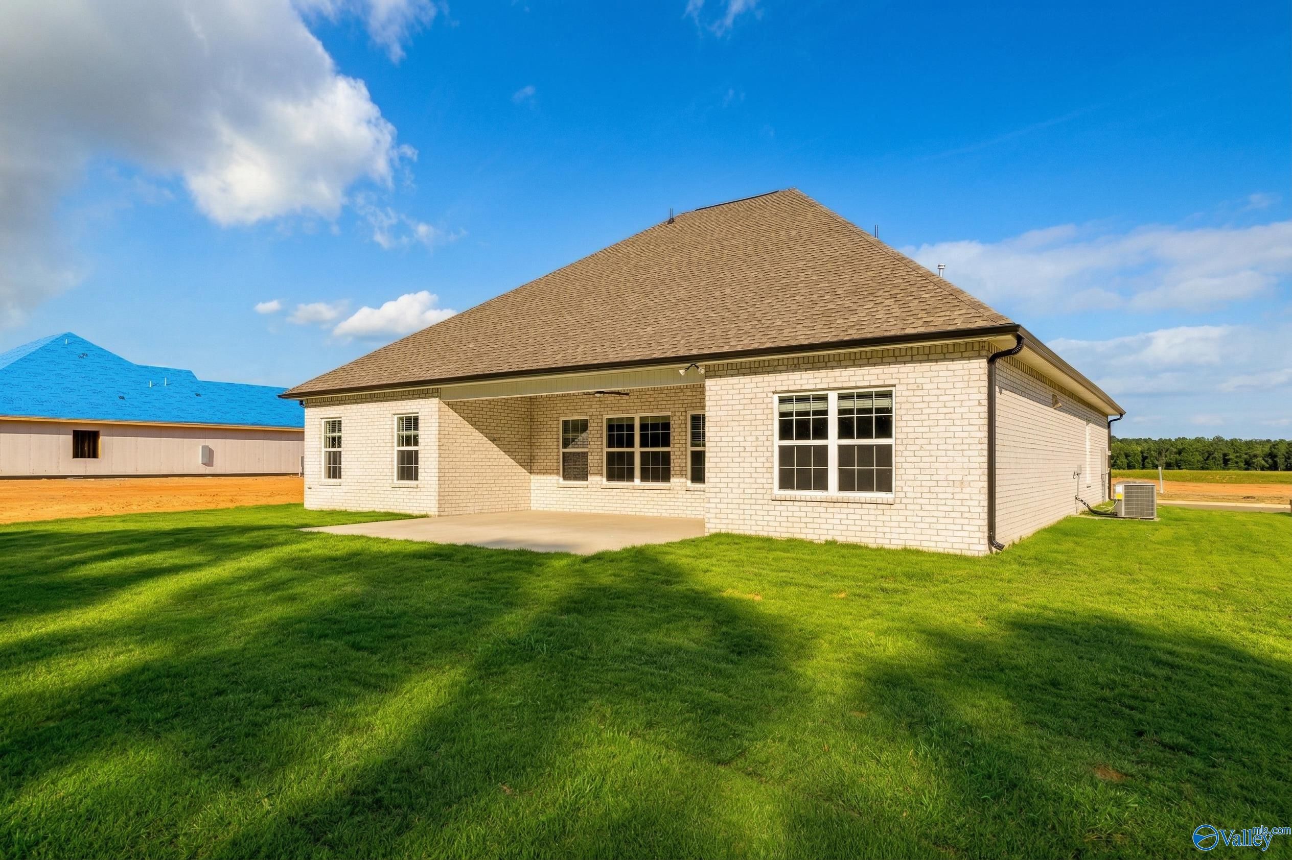 Rear view of Davidson Homes The Rockford 3-bedroom brick house with covered patio and lush green yard in Cain Park, Hartselle, Alabama