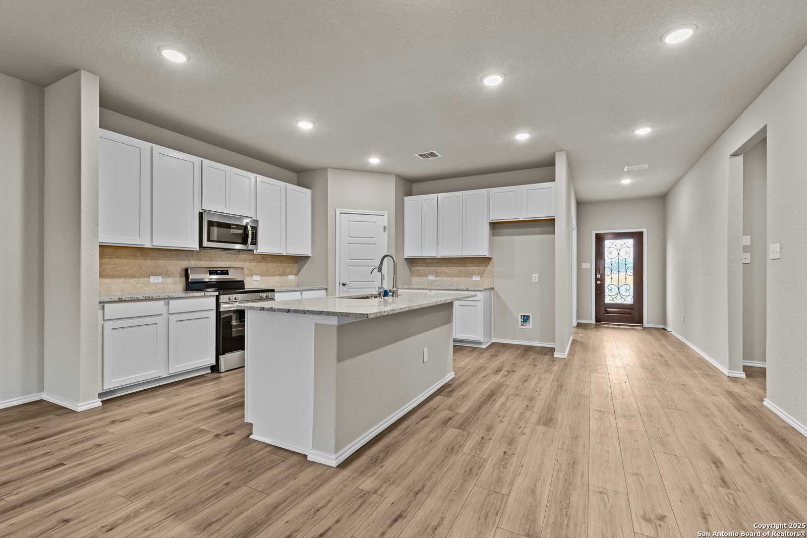 Spacious modern kitchen with white cabinets, granite island, stainless appliances in Davidson Homes The Douglas F, San Antonio