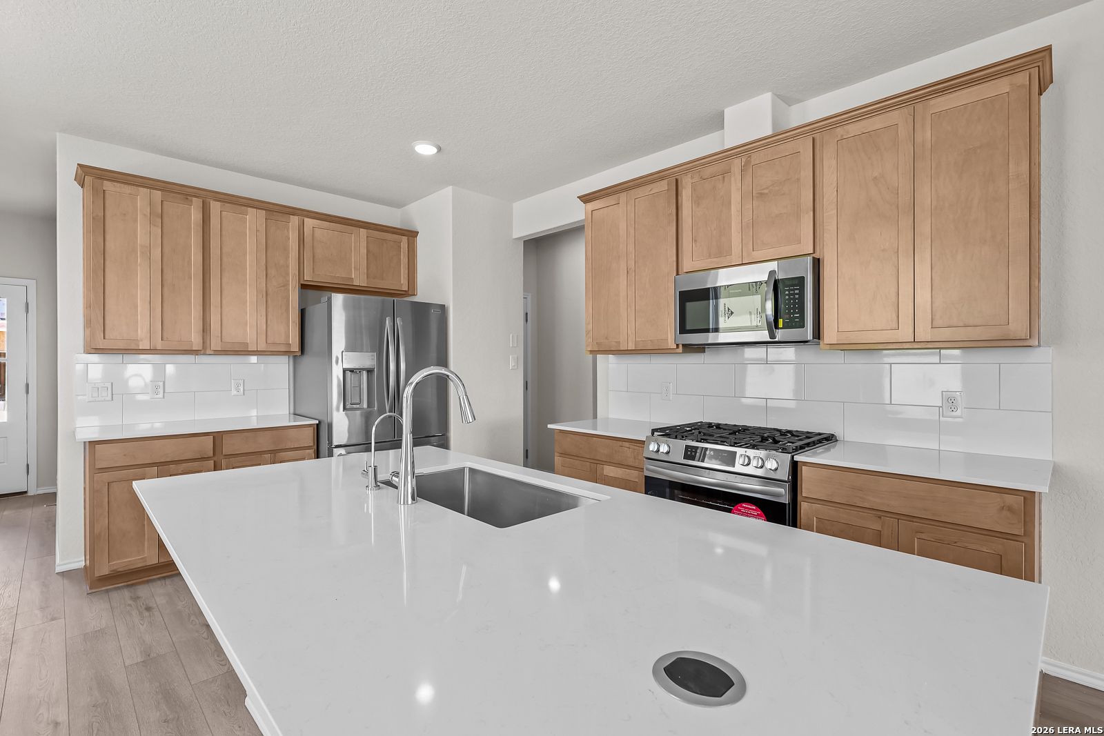 Modern kitchen with white quartz island, stainless steel appliances, and wood cabinets in The Gillian B floor plan.