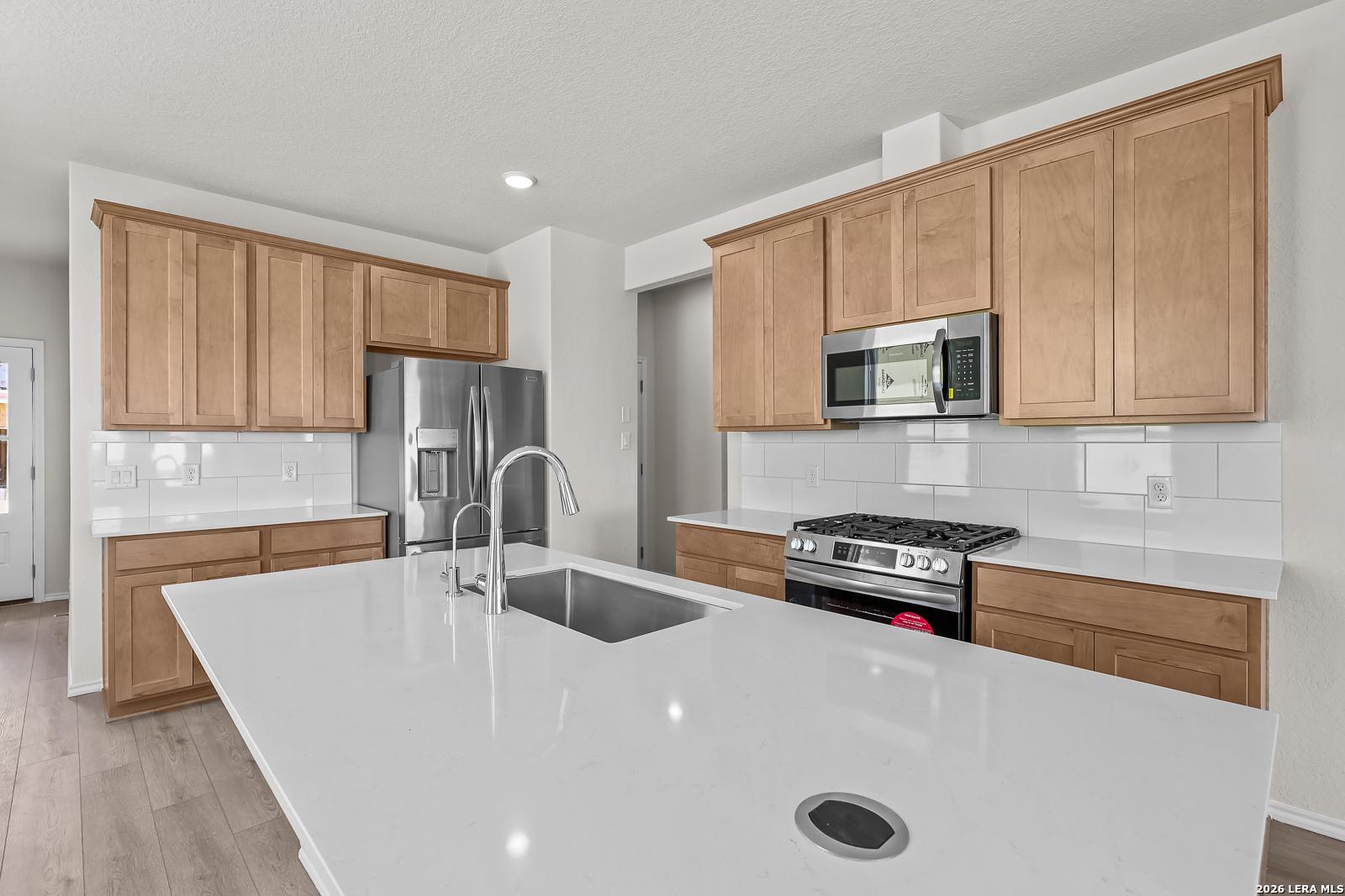 Modern kitchen with white quartz island, stainless steel appliances, and wood cabinets in The Gillian B floor plan.