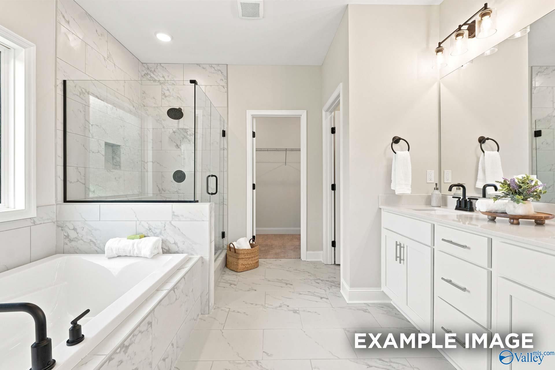 Modern primary bathroom with marble tile, soaking tub, glass shower, and dual vanity in The Montgomery B, Athens, Alabama.