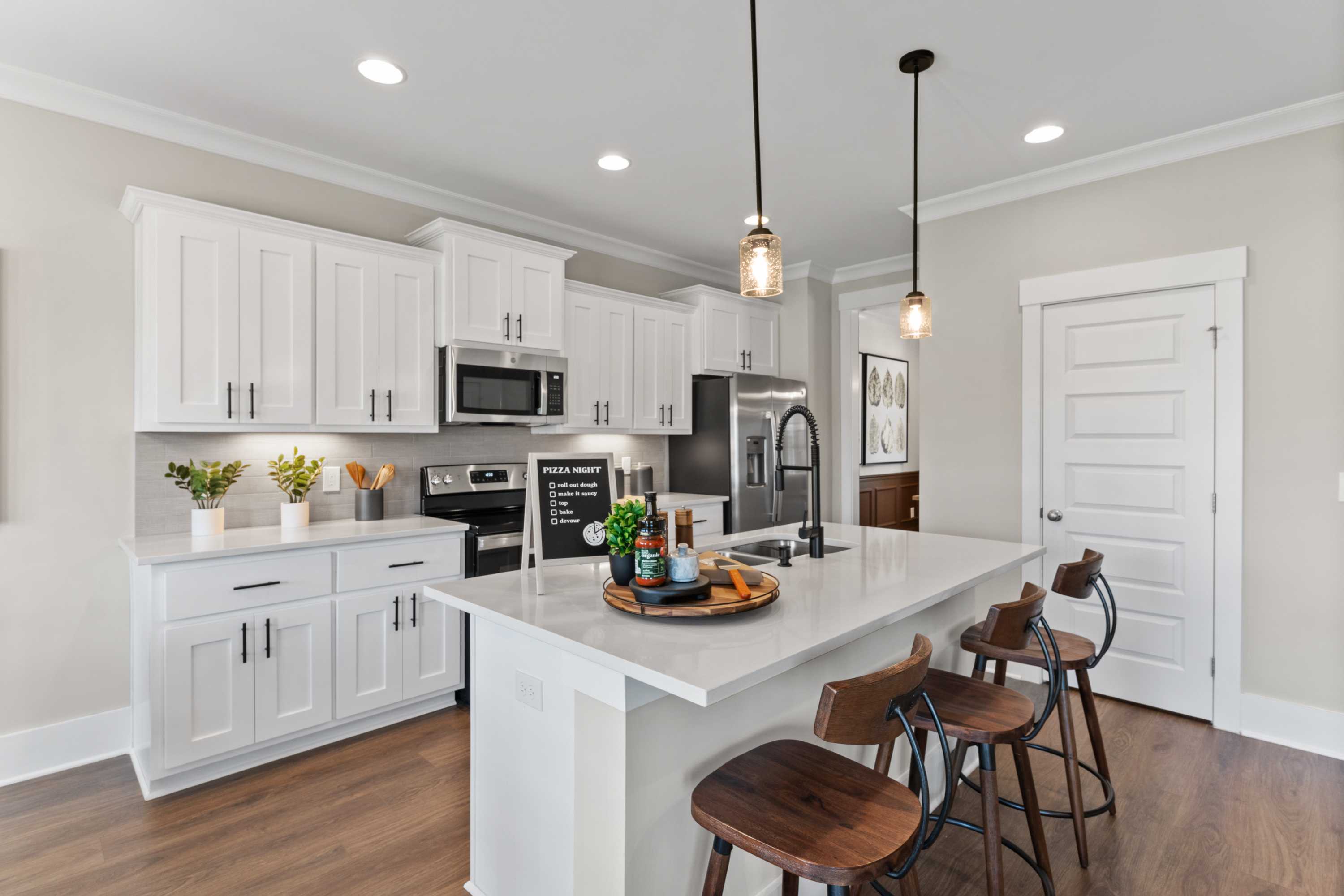 Spacious kitchen in The Shelby B featuring white shaker cabinets, large island with wood stools, stainless appliances