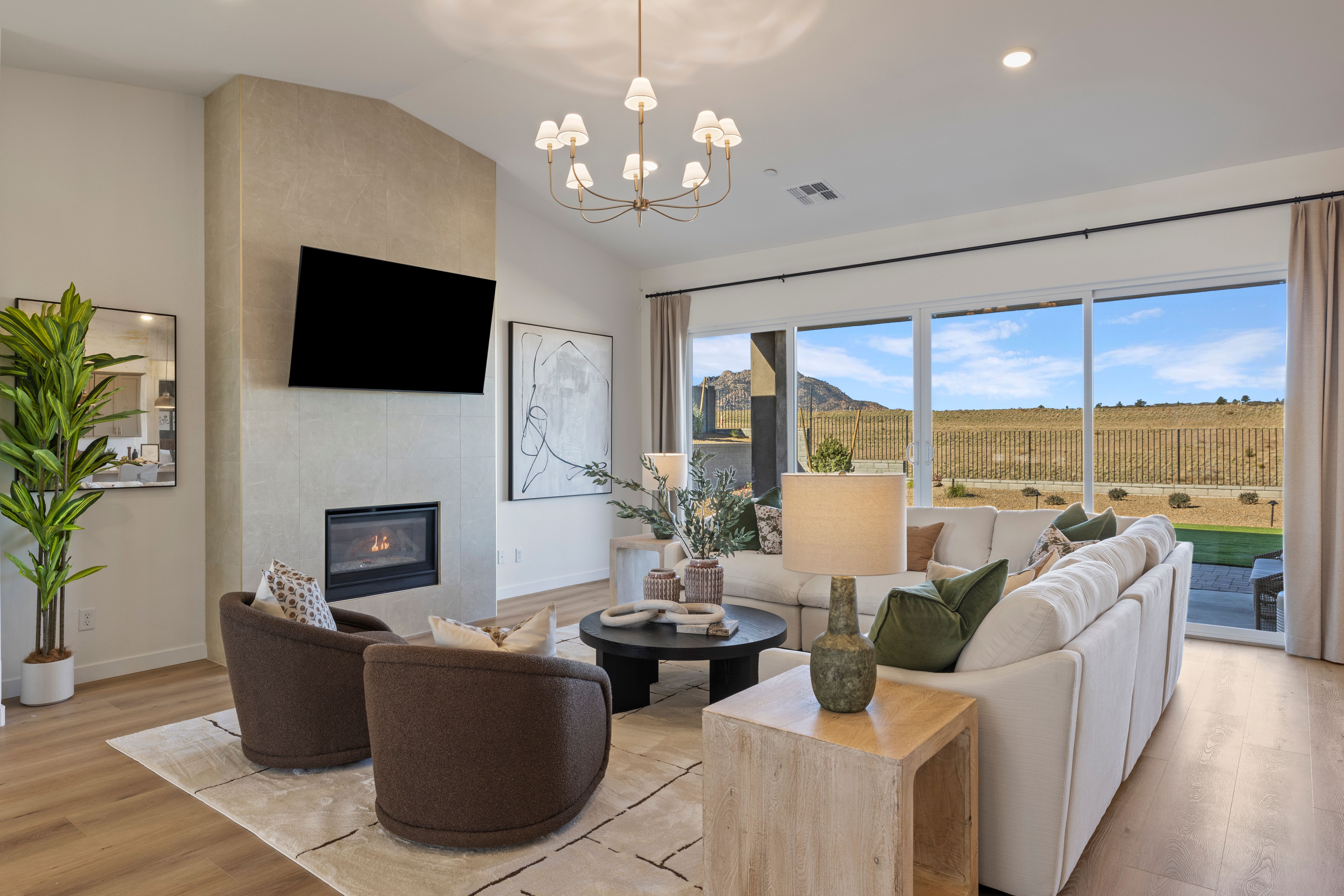 Cozy living room in Hidden Hills Prescott AZ by Davidson Homes with stone fireplace, modern seating, chandelier, and mountain views through sliding doors