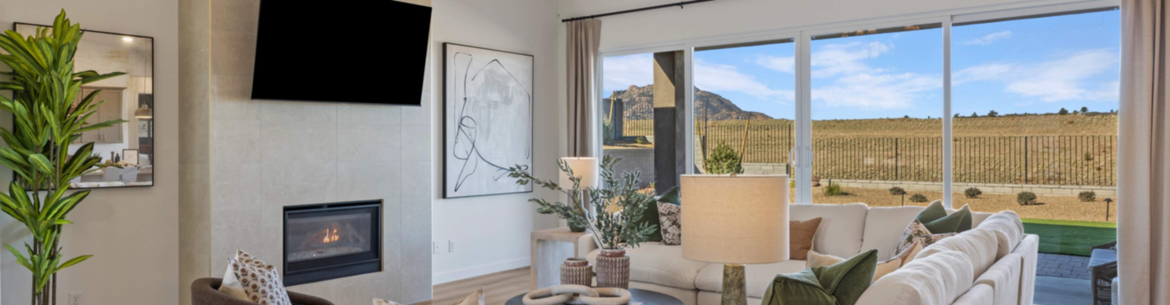 Modern living room in new Cottonwood home with beige sofa, lit fireplace, chandelier, and desert mountain view through large windows