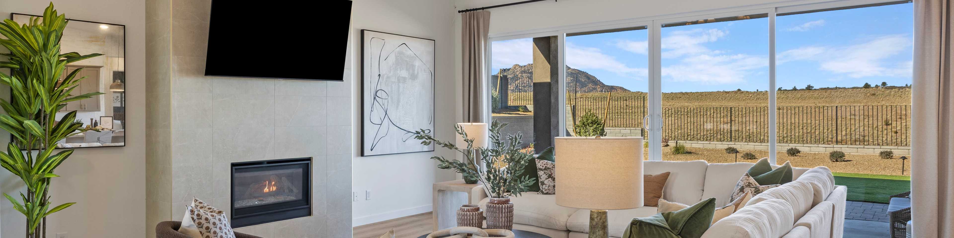 Modern living room in new Cottonwood home with beige sofa, lit fireplace, chandelier, and desert mountain view through large windows