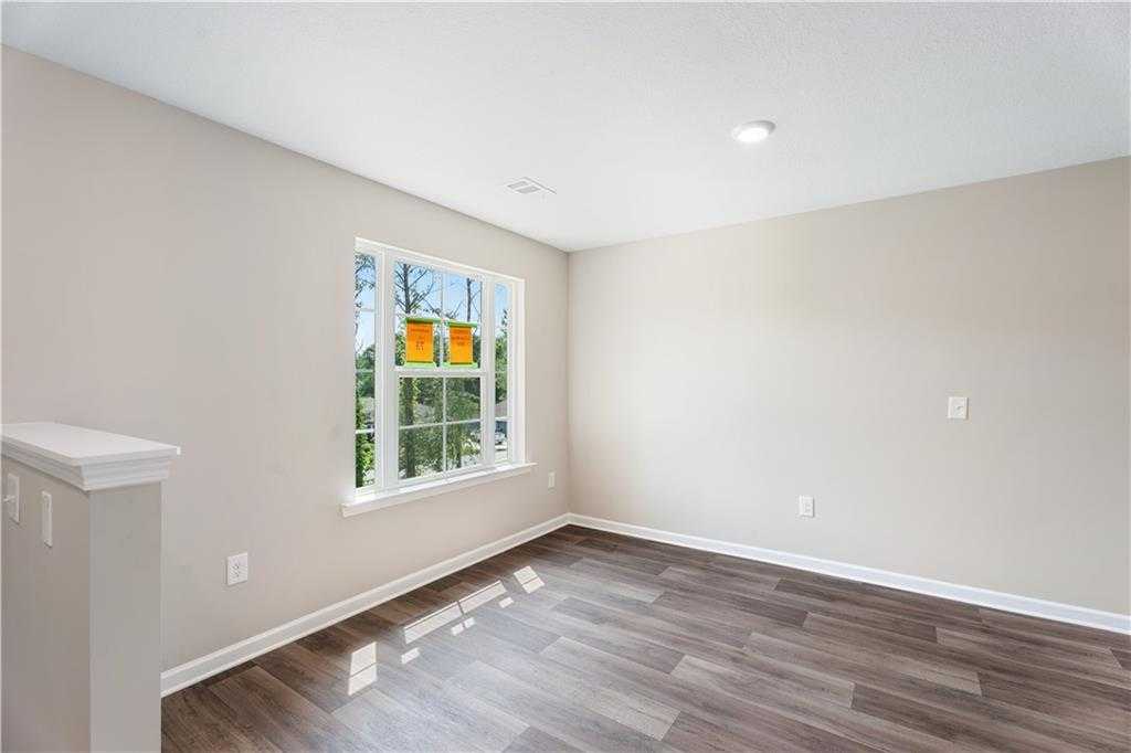 Bright bedroom with beige walls, large window with orange blinds, and hardwood floors in Evermore Homes The Washington, Phenix City, Alabama