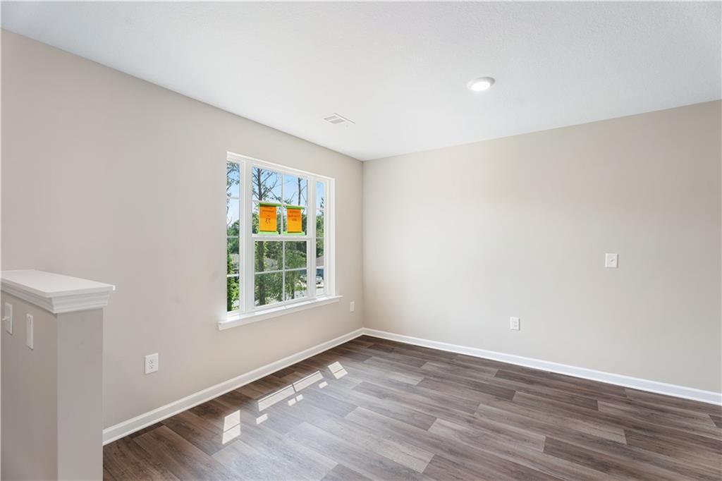 Bright bedroom with beige walls, large window with orange blinds, and hardwood floors in Evermore Homes The Washington, Phenix City, Alabama