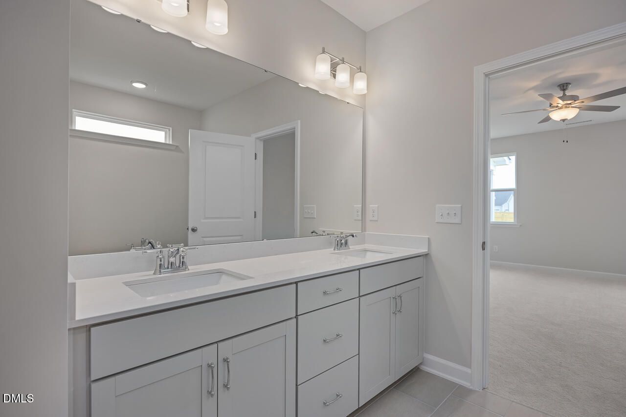 Modern double vanity bathroom with white quartz counters, cabinets, and large mirror in Davidson Homes The Cypress D II, Angier, NC
