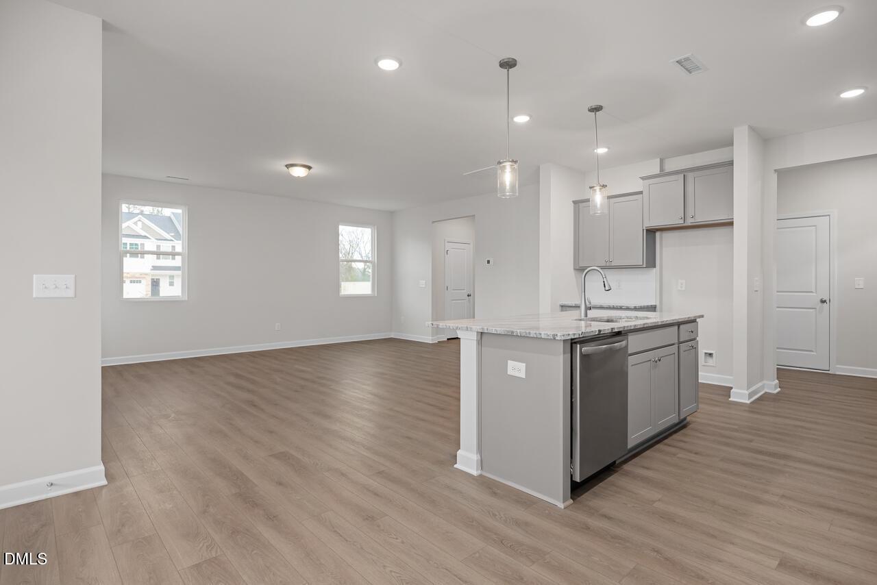 Modern open kitchen with quartz island, stainless dishwasher, gray cabinets, and hardwood floors in The Gavin B, Lillington home