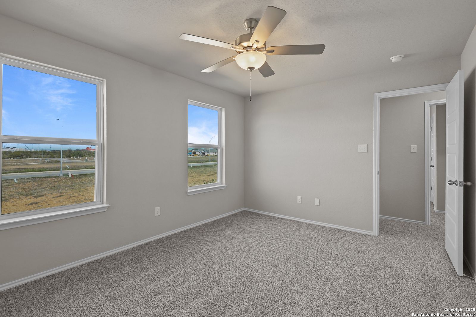 Bright secondary bedroom featuring light gray walls, large windows with scenic field view, ceiling fan in Davidson Homes The Trinity D, San Antonio