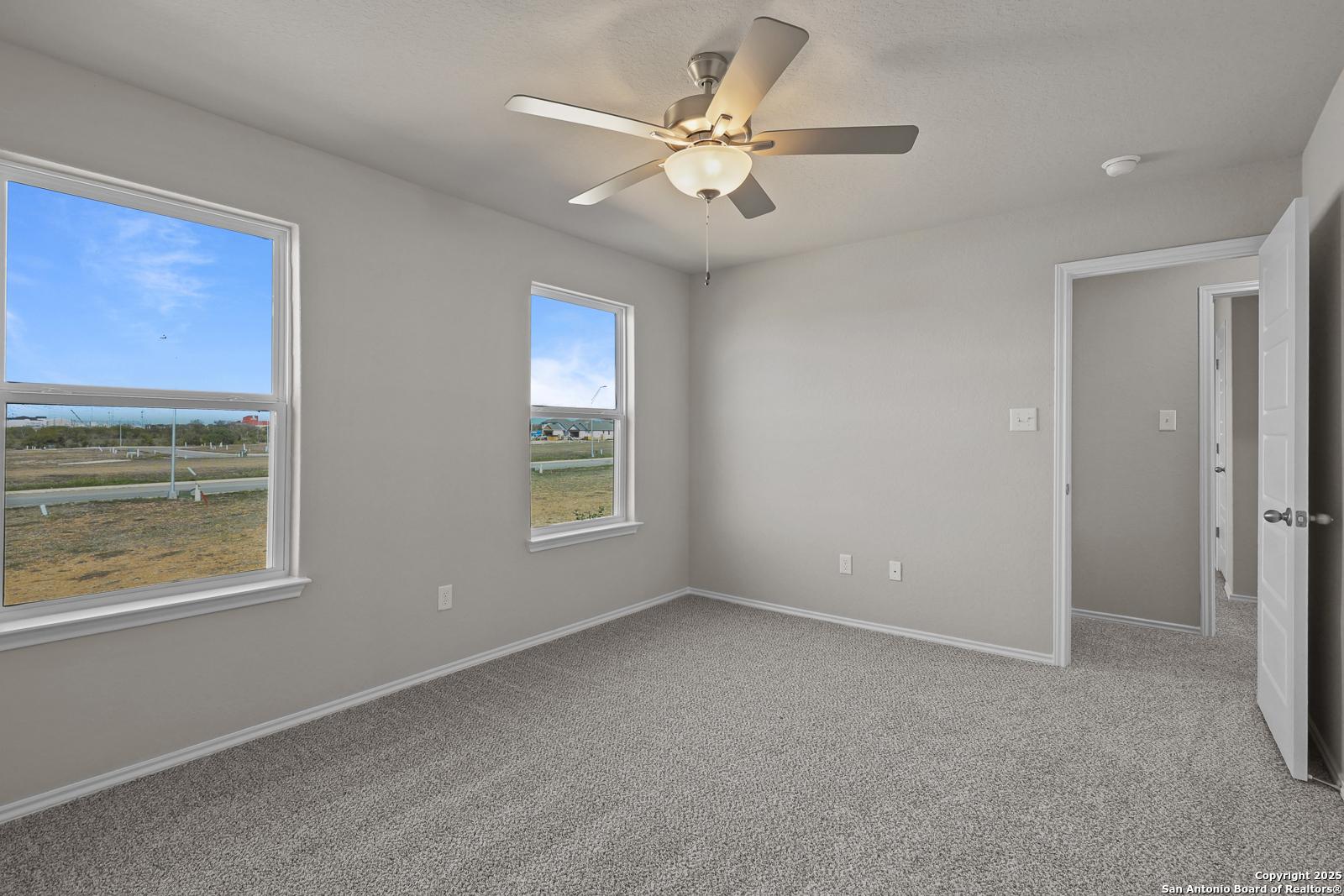 Bright secondary bedroom featuring light gray walls, large windows with scenic field view, ceiling fan in Davidson Homes The Trinity D, San Antonio