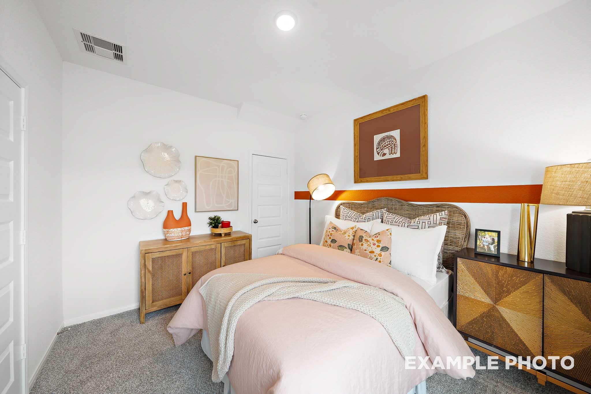 Cozy secondary bedroom in The Sabine E with pink bedding, wooden dresser, wall art, and modern lamps