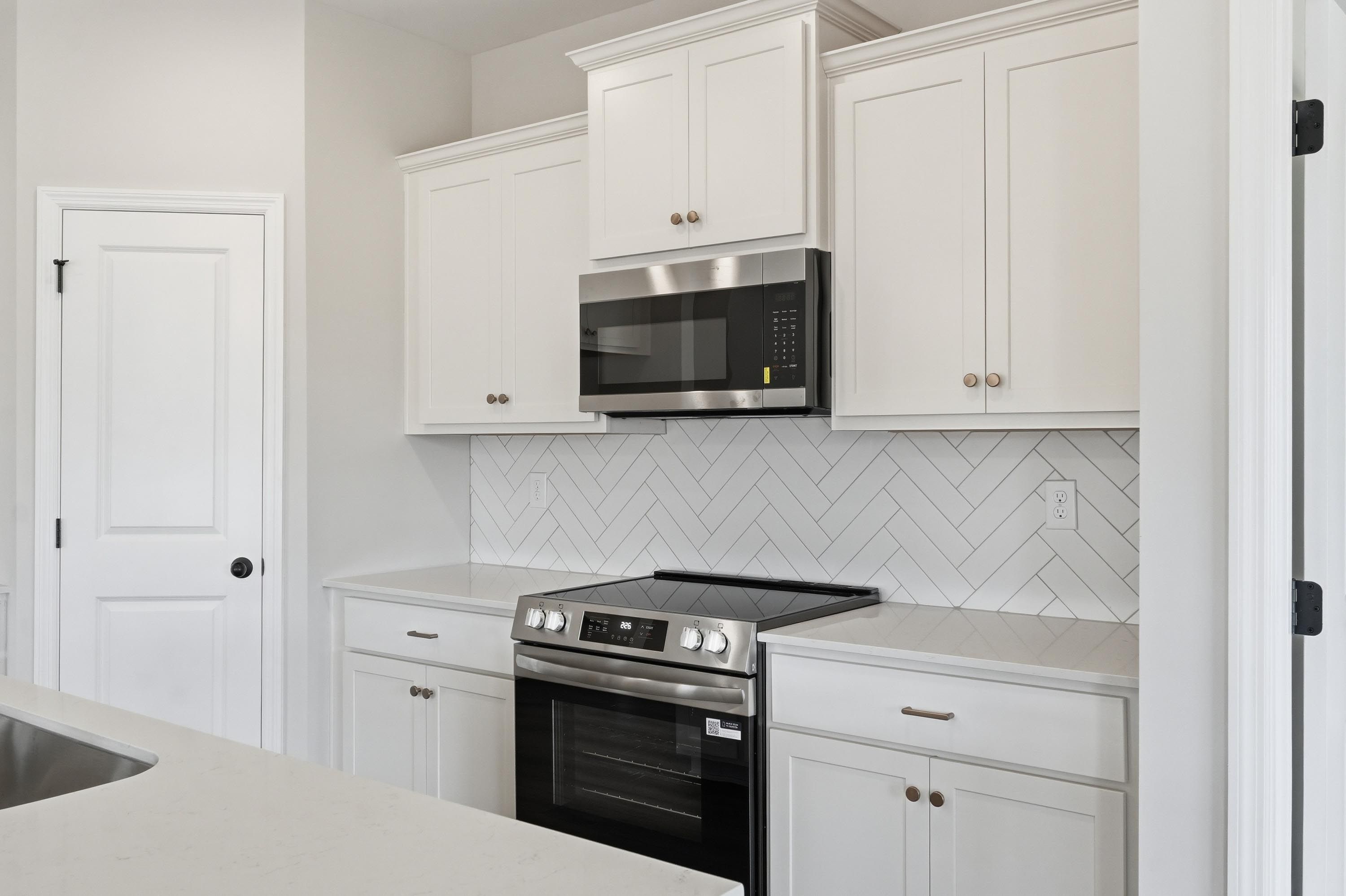 Modern kitchen in The Glen A featuring white cabinets, stainless steel appliances, and a herringbone tile backsplash.