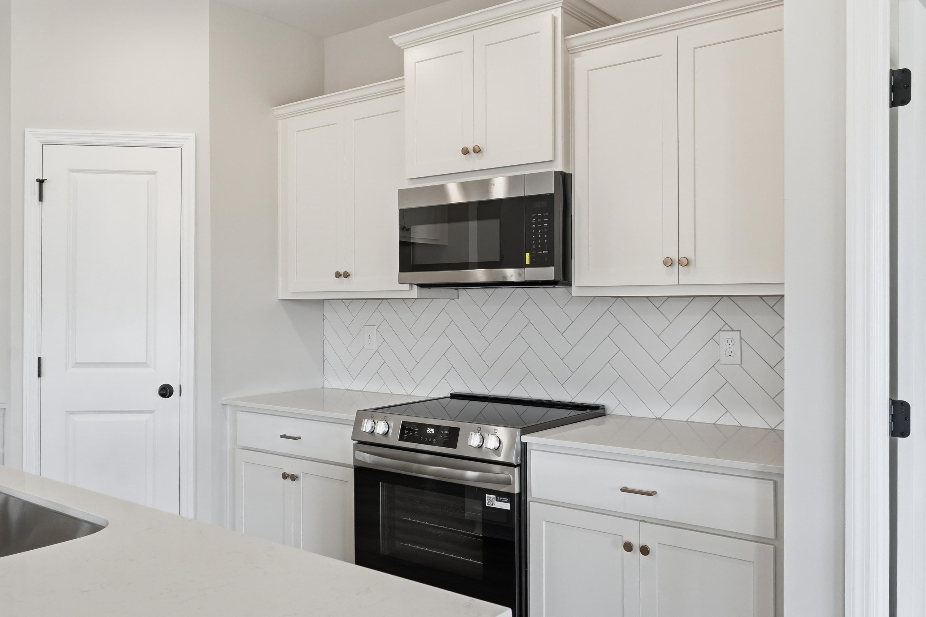Modern kitchen in The Glen A featuring white cabinets, stainless steel appliances, and a herringbone tile backsplash.