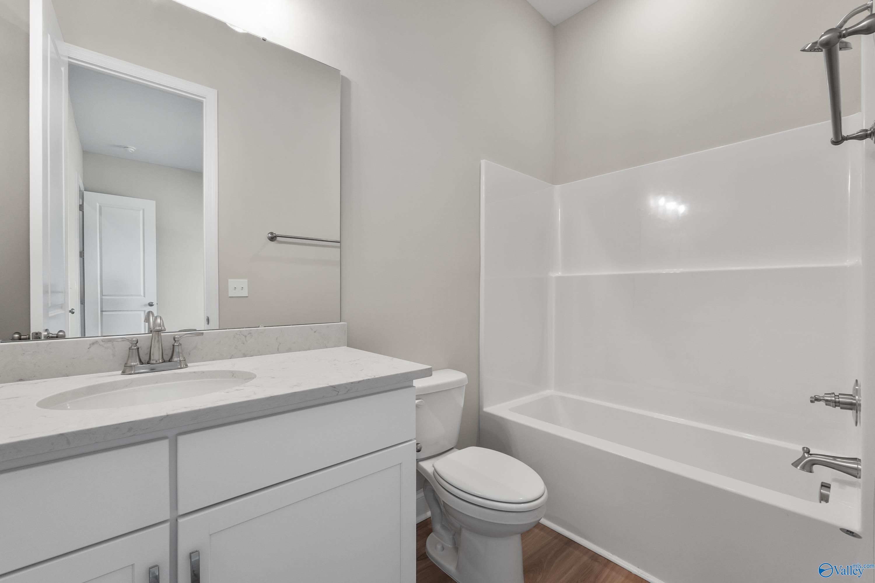 Modern guest bathroom featuring white vanity, sink, mirror, toilet, and tub-shower combo in Evermore Homes The Haven, Owens Cross Roads, Alabama