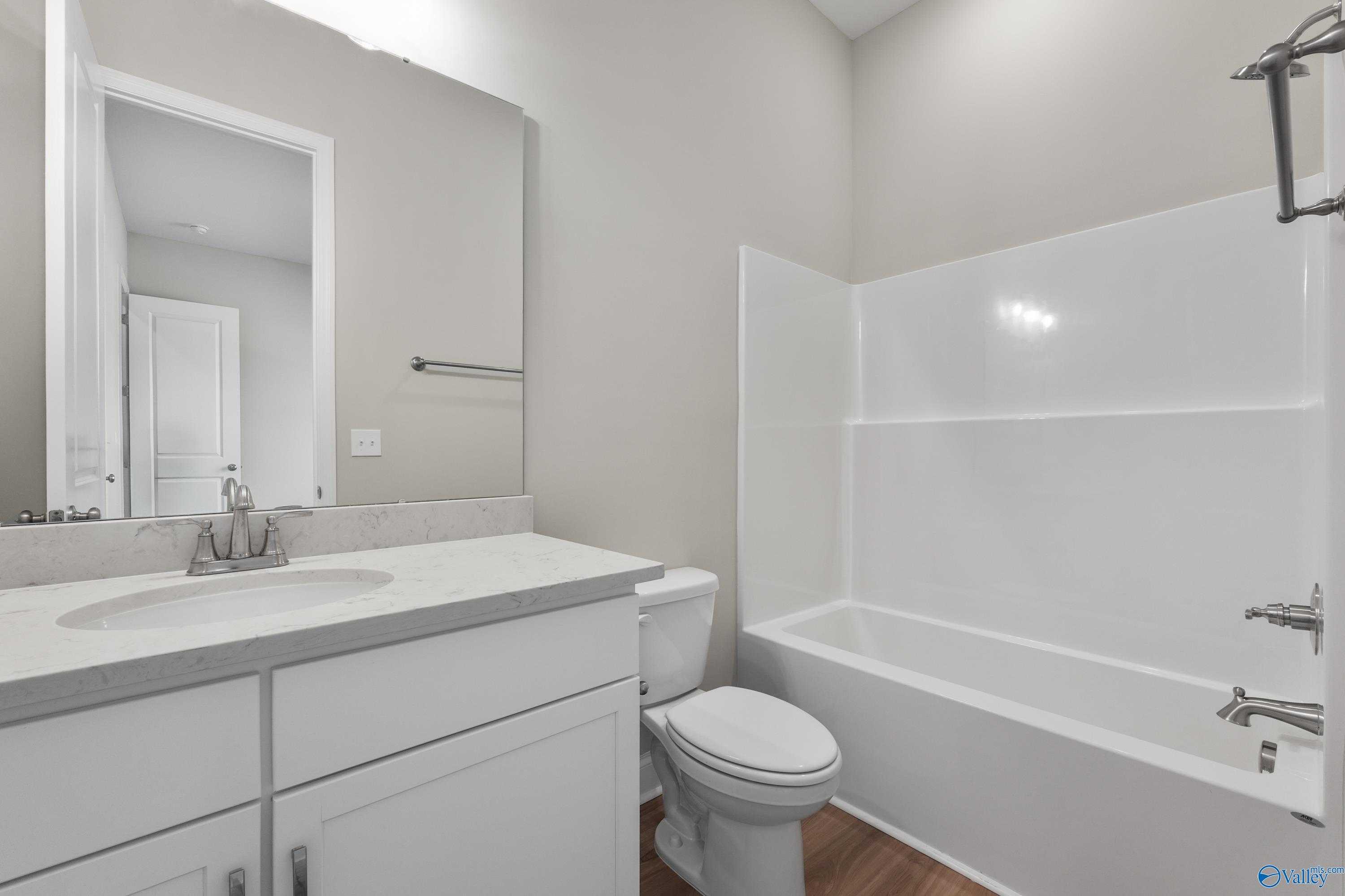 Modern guest bathroom featuring white vanity, sink, mirror, toilet, and tub-shower combo in Evermore Homes The Haven, Owens Cross Roads, Alabama