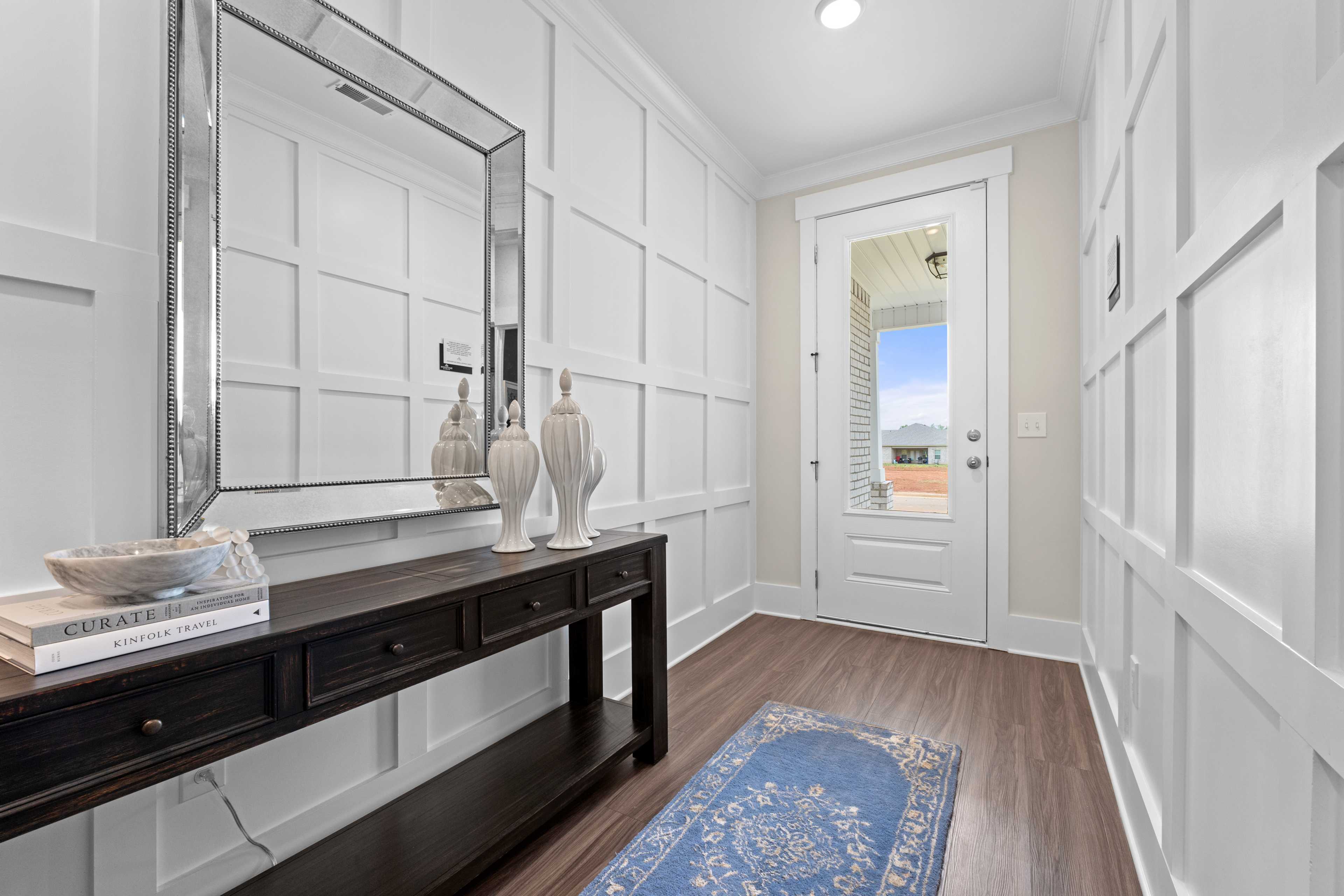 Elegant entryway hallway at Ivy Hills in Toney Alabama with white wainscoting, dark console table, silver mirror, and blue rug