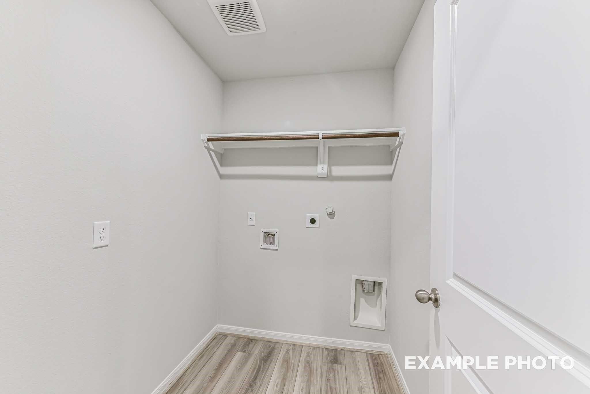 Bright laundry room with built-in shelves, washer-dryer hookups, and white walls in Davidson Homes The Riviera A, Sierra Vista, Rosharon, Texas