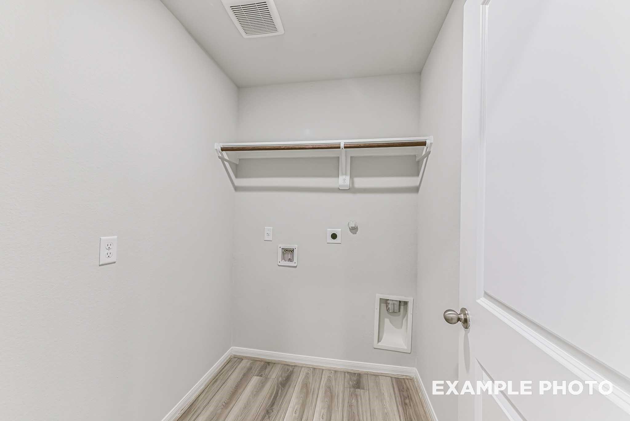 Bright laundry room with built-in shelves, washer-dryer hookups, and white walls in Davidson Homes The Riviera A, Sierra Vista, Rosharon, Texas