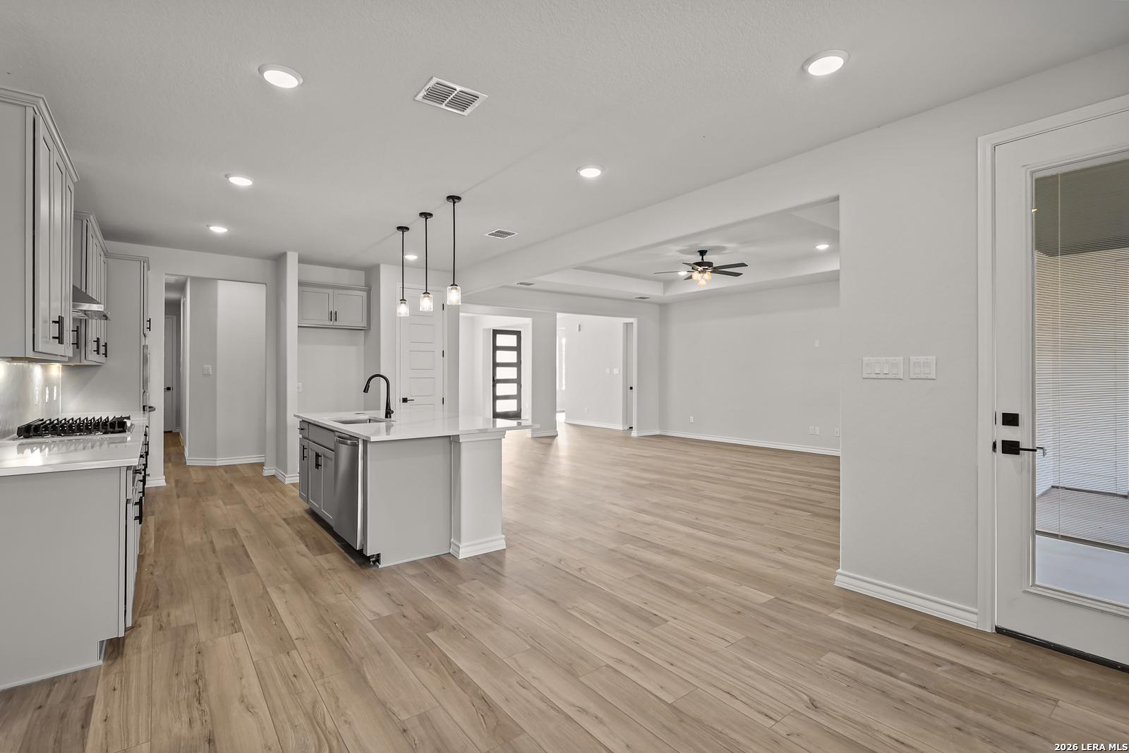 Open-concept kitchen with island and pendant lights flowing into spacious living area in Davidson Homes Oxford F, Castroville, TX
