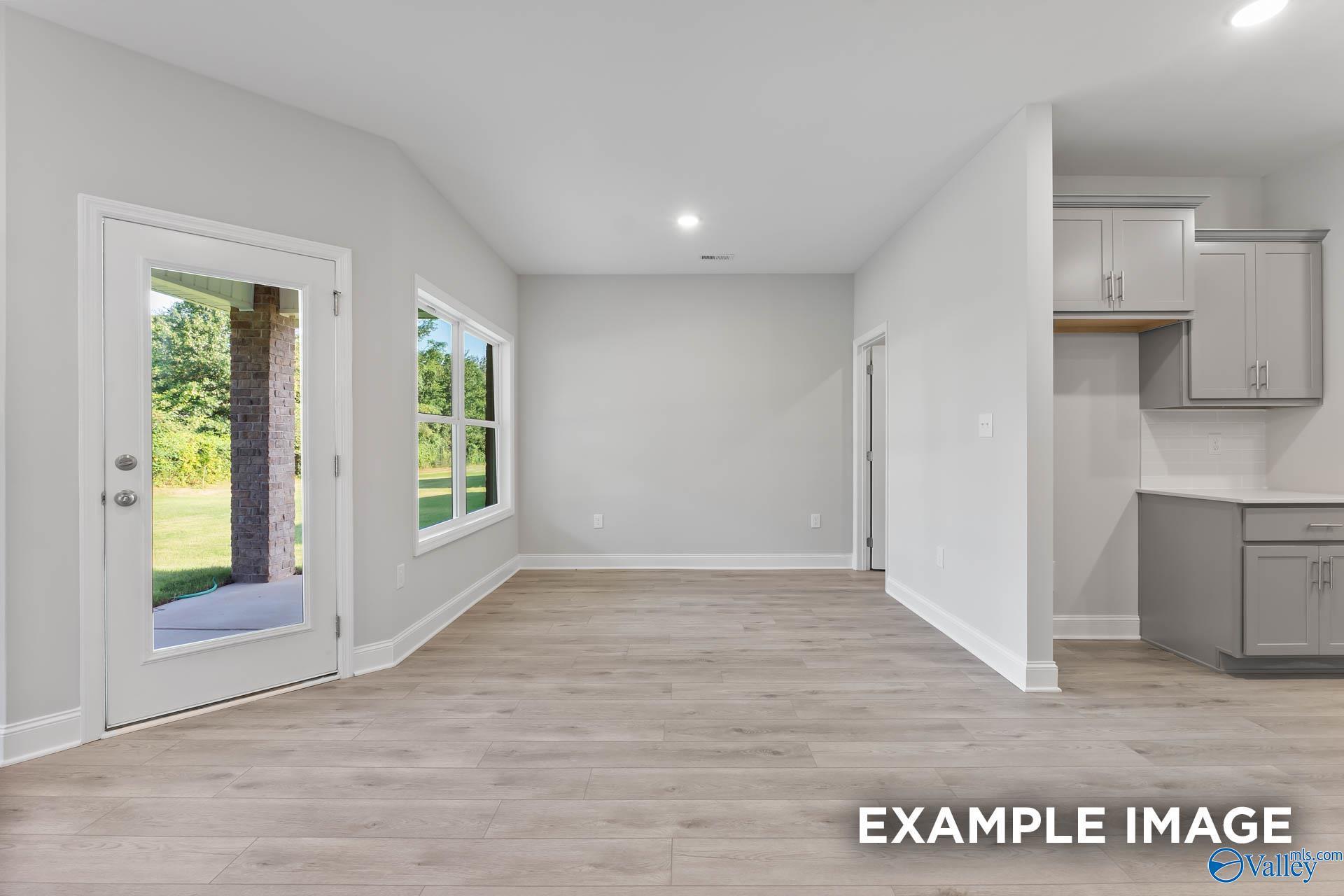 Open living area with light hardwood floors, gray walls, large windows, and backyard view in The Daphne F 4-bedroom home, Hazel Green AL