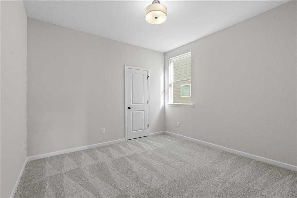 Spacious empty bedroom with neutral gray walls, patterned carpet, white door, and window in Davidson Homes The Edison A, Loganville, GA