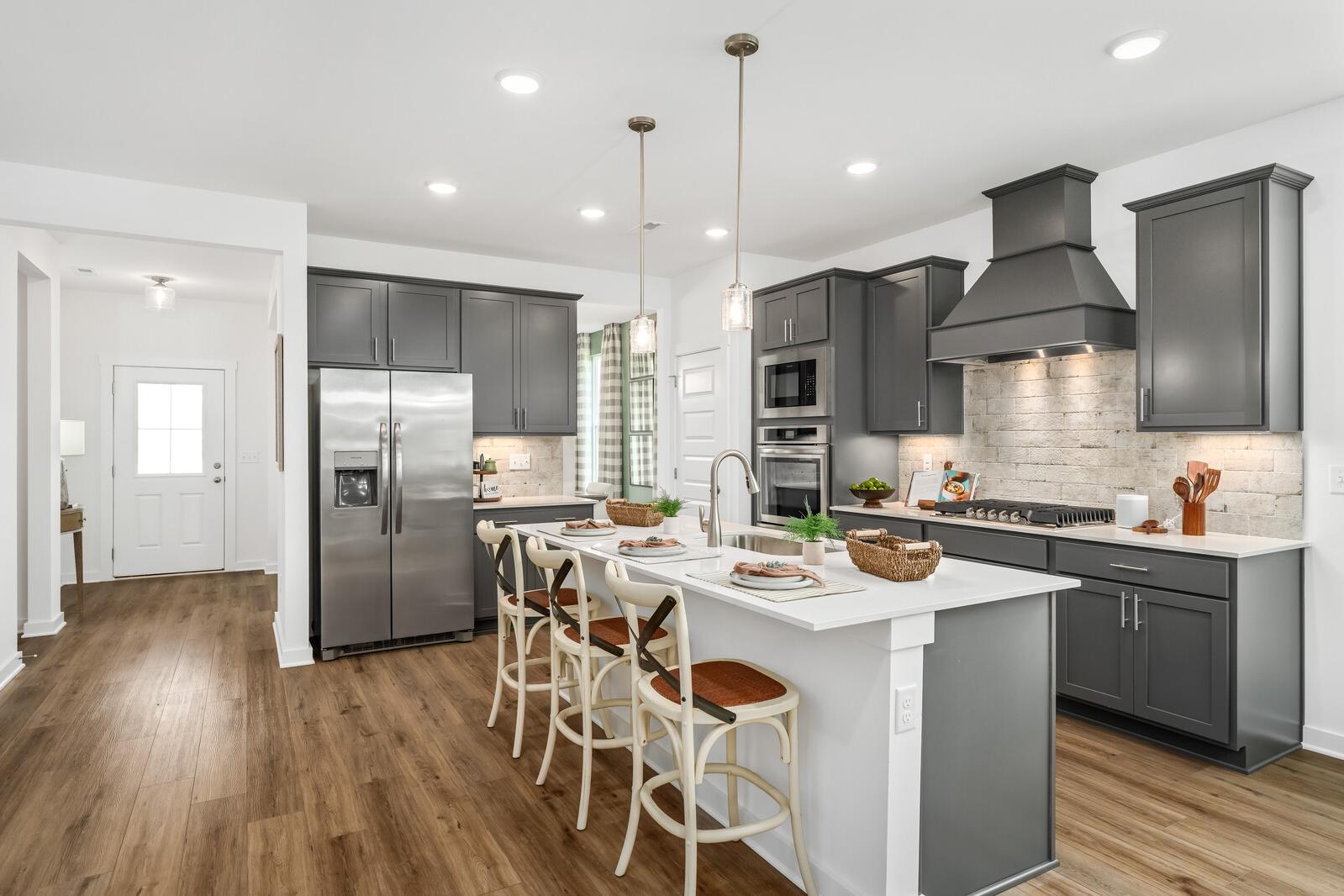Modern kitchen with gray cabinets, white island, stainless appliances, and hardwood floors at Calista Farms in White House, TN