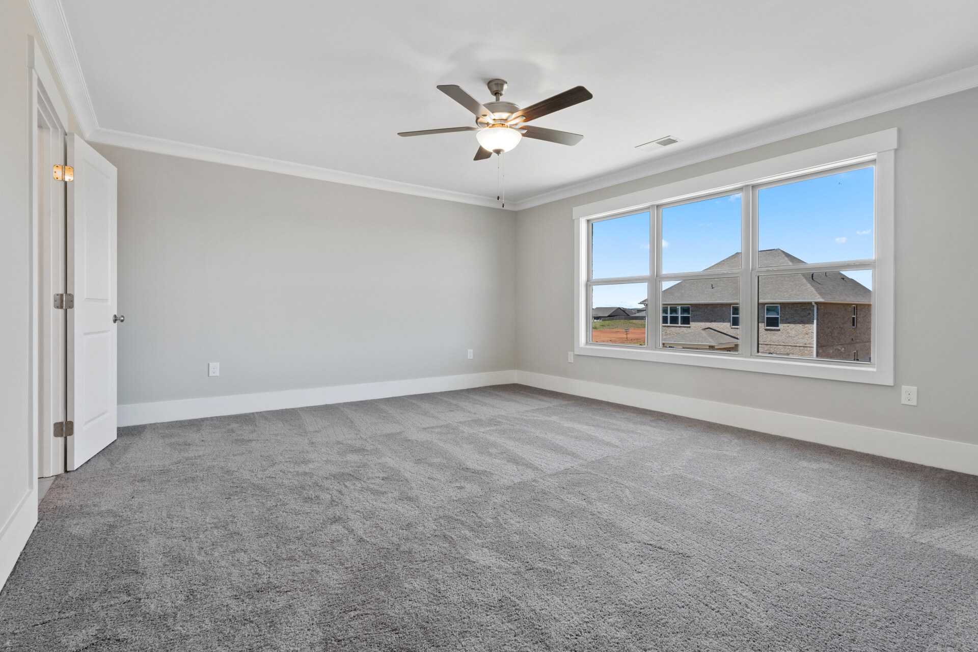 Empty bedroom in Little Burwell Estates, Harvest Alabama with gray walls, carpet, ceiling fan, and large windows overlooking neighborhood
