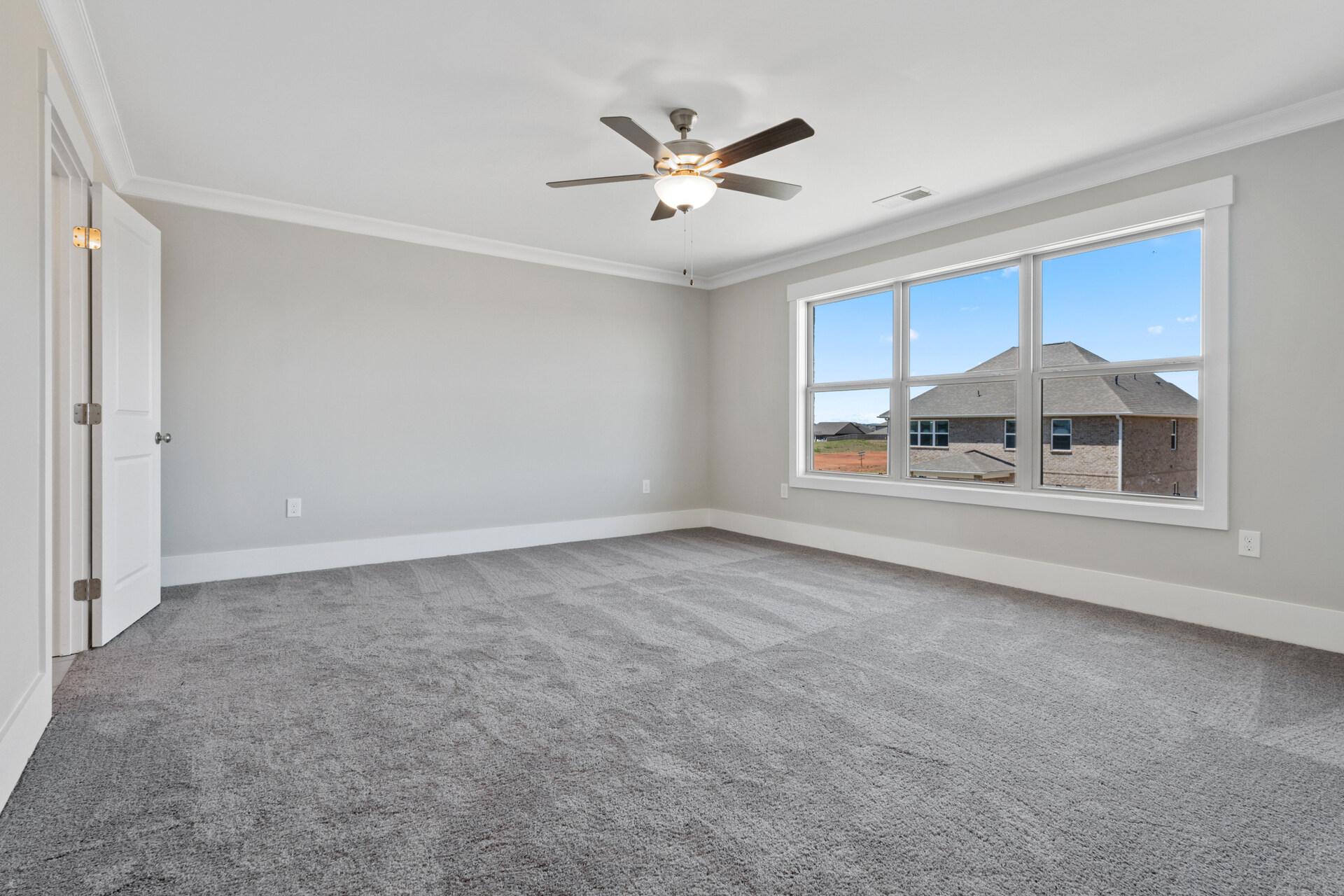 Empty bedroom in Little Burwell Estates, Harvest Alabama with gray walls, carpet, ceiling fan, and large windows overlooking neighborhood
