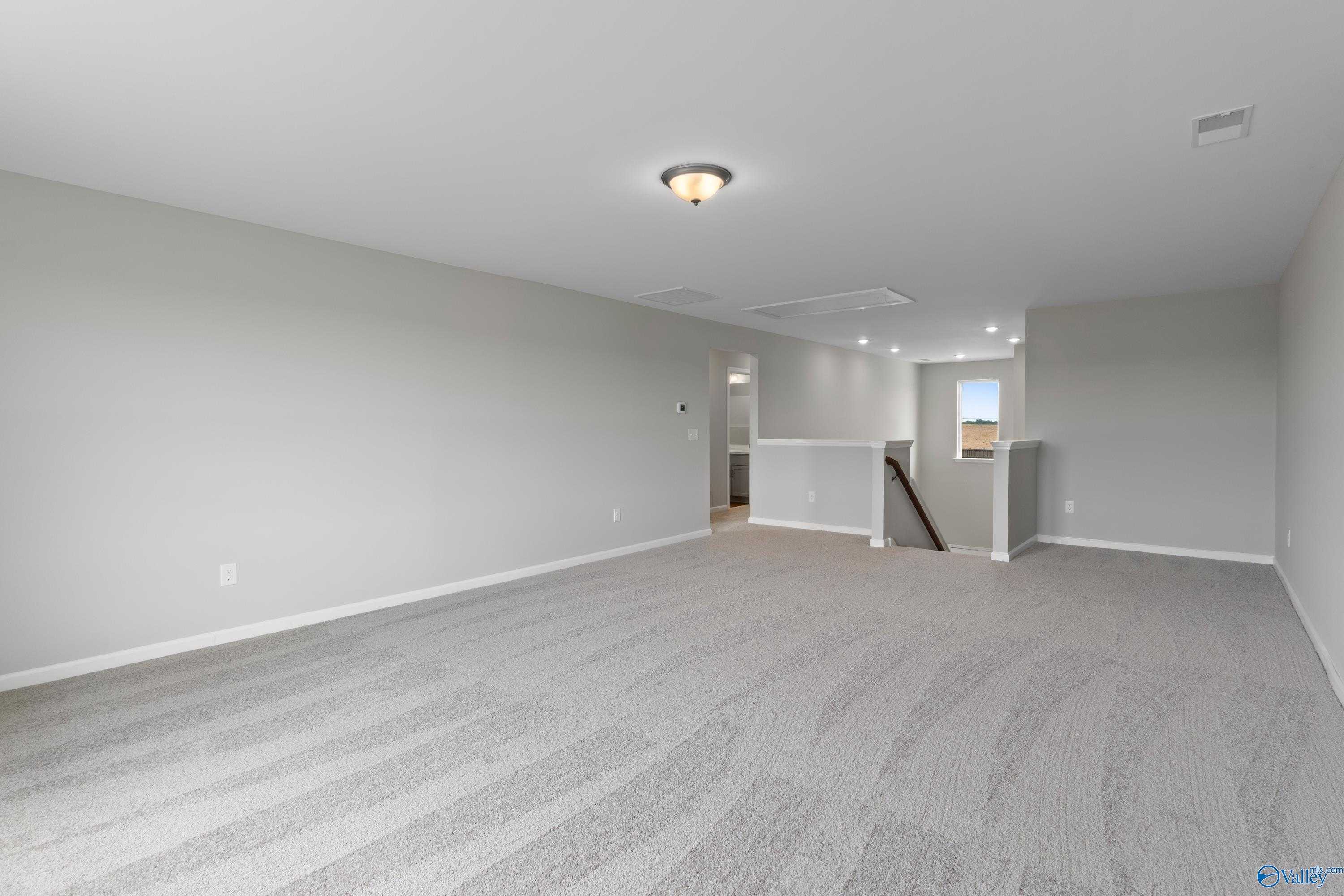 Spacious upstairs bonus room with gray carpet, neutral walls, and open staircase in Davidson Homes The Dorado, Athens Alabama
