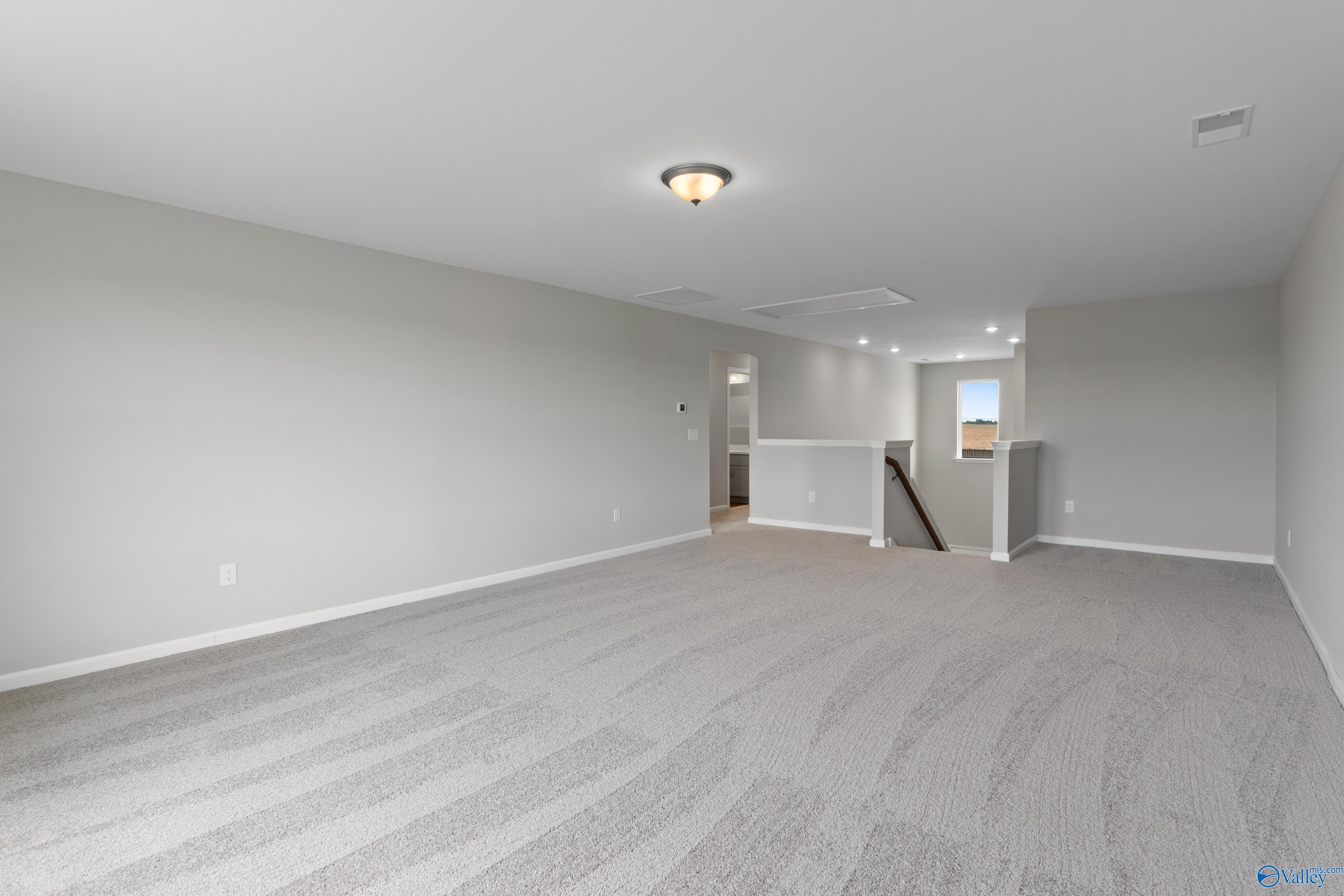 Spacious upstairs bonus room with gray carpet, walls, and staircase in Davidson Homes Dorado floor plan, Athens Alabama