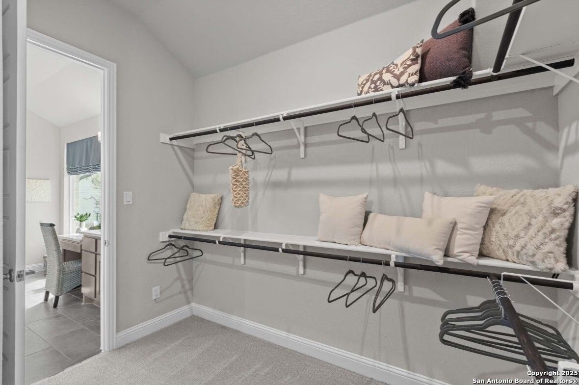 Spacious walk-in closet with white shelving, hanging rods, and neutral pillows in Davidson Homes The Garner B, Ladera, San Antonio