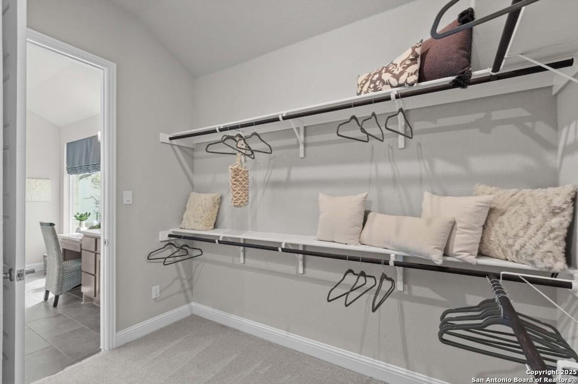 Spacious walk-in closet with white shelving, hanging rods, and neutral pillows in Davidson Homes The Garner B, Ladera, San Antonio