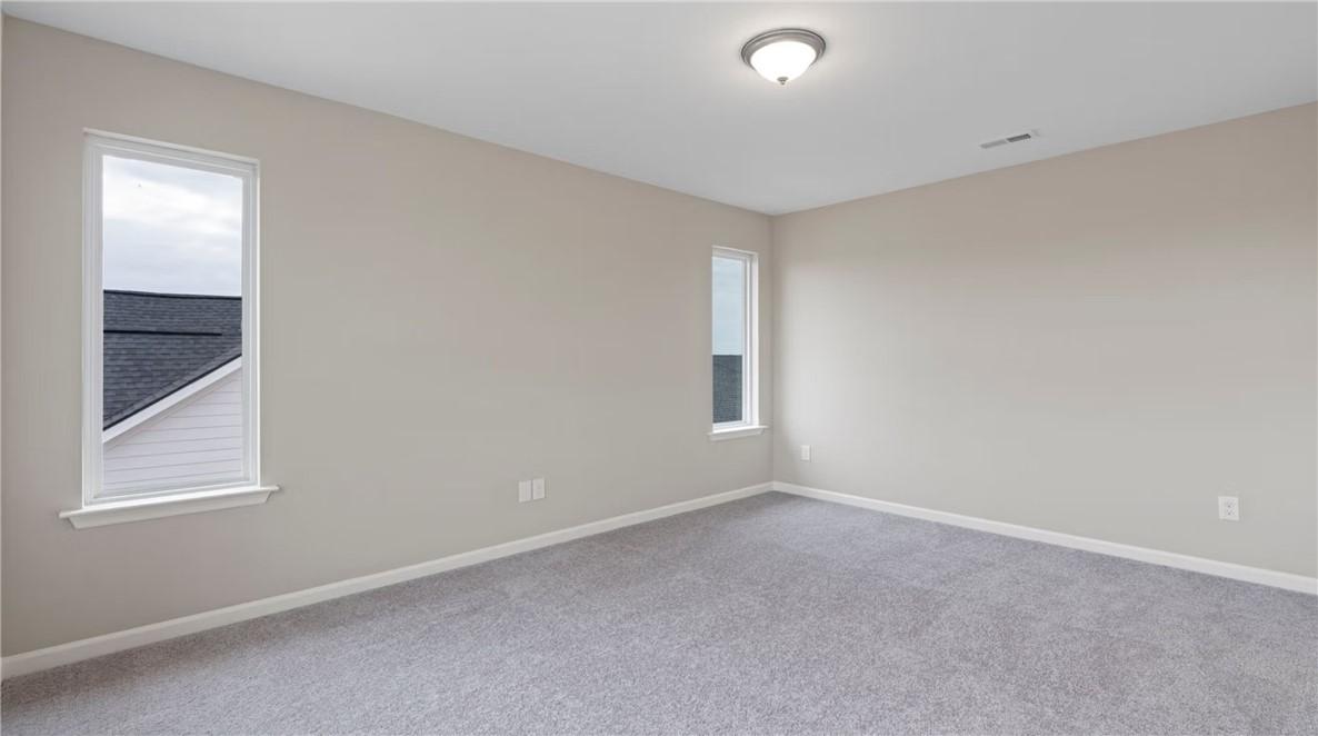 Empty beige bedroom with large window overlooking roof, carpet floor in Evermore Homes The Stella D, Cusseta, Alabama