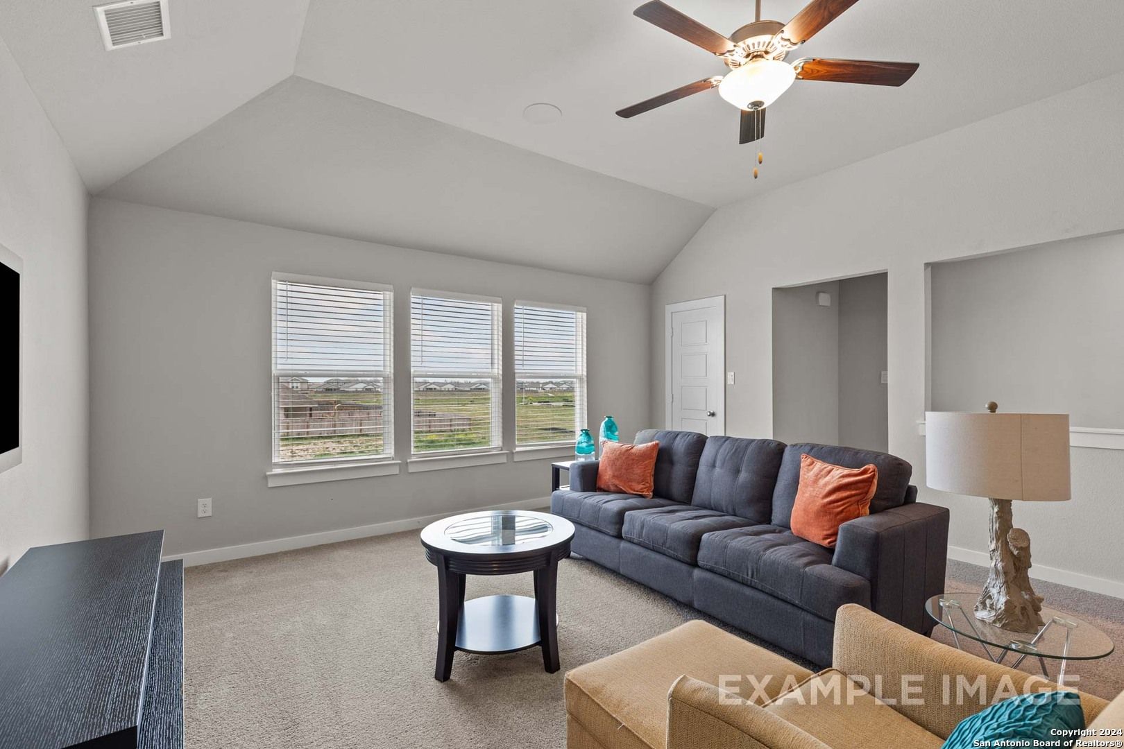 Cozy living room with vaulted ceiling, ceiling fan, large windows overlooking fields, gray sectional sofa in The Collin A, Davidson Homes, Seguin TX